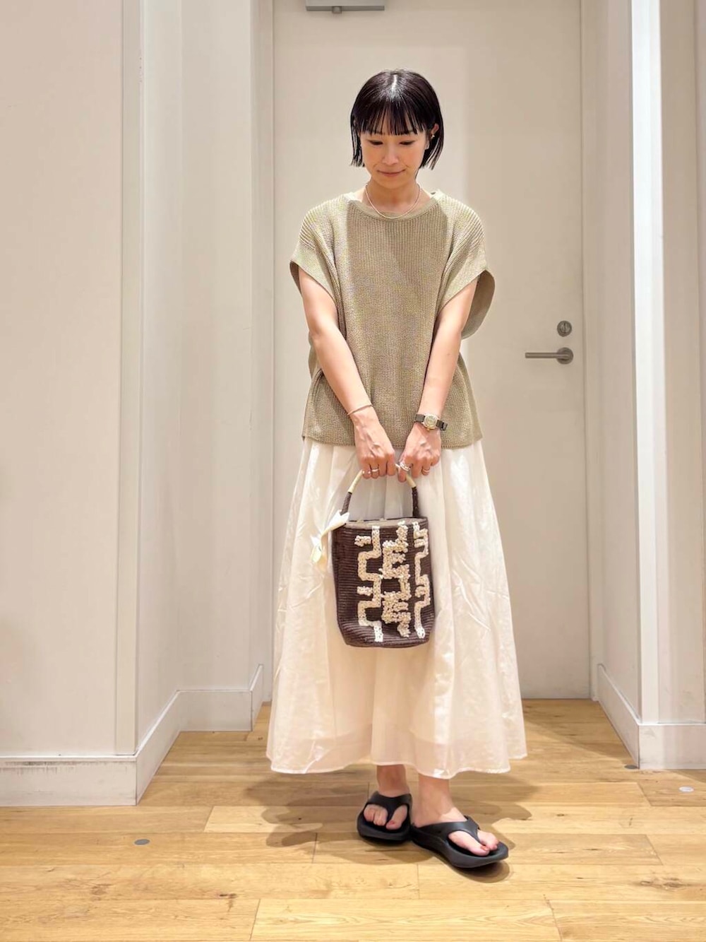 ブラック系のサンダル、ブラウン系のショルダーバッグ、ホワイト系のワンピースを着用したレディースの夏コーディネートの2枚目の写真