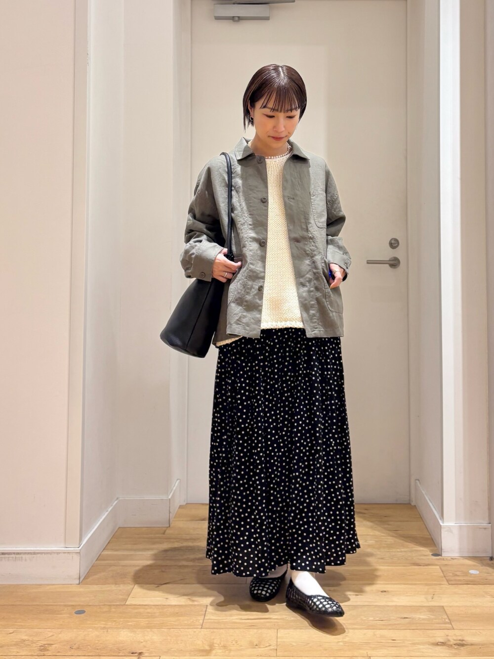 グレー系のカバーオール、ホワイト系のベスト、ブラック系のスカートを着用したレディースの春コーディネートの3枚目の写真