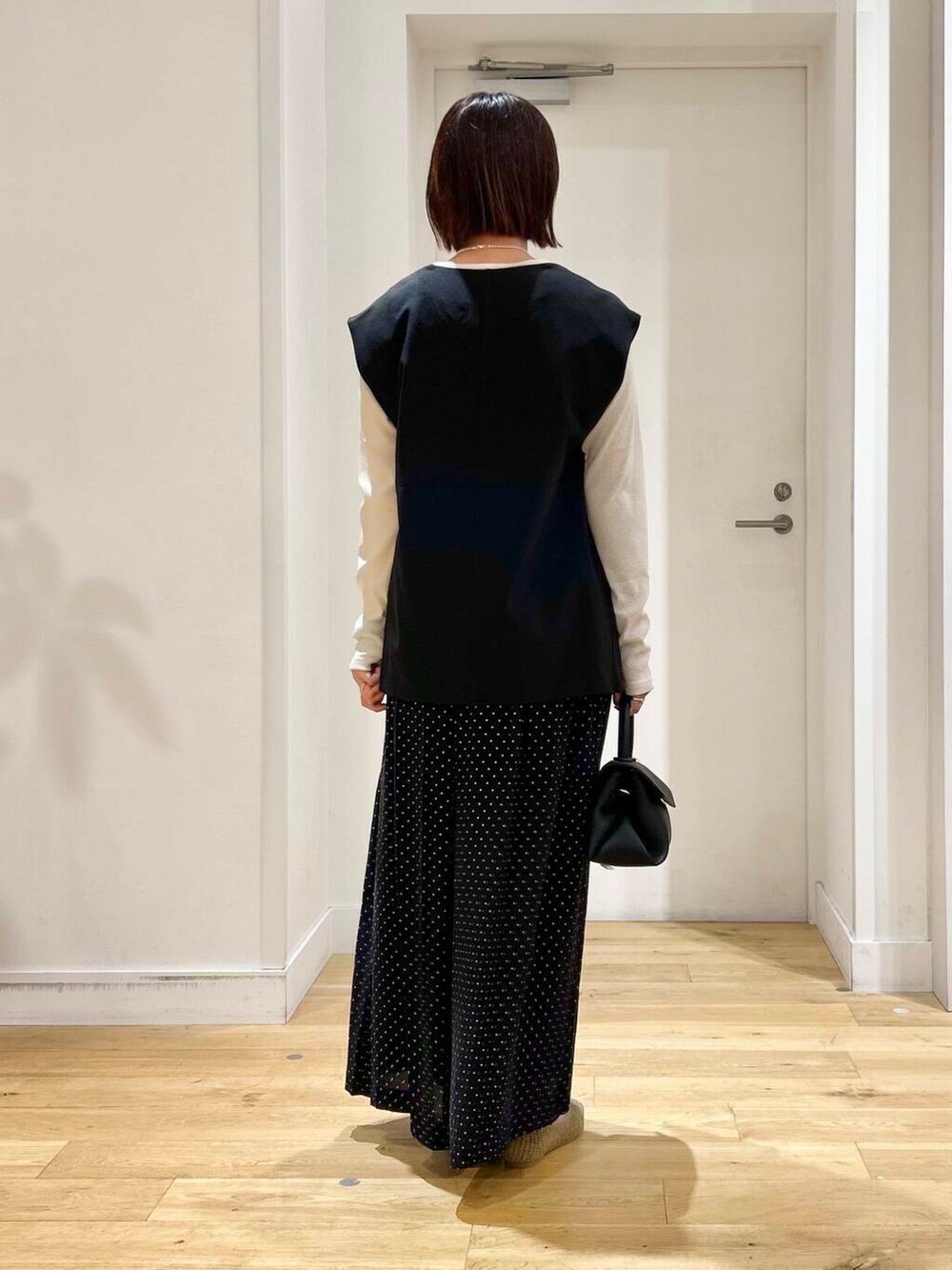 ベージュ系のパンプス、ブラック系のベスト、ブラック系のショルダーバッグを着用したレディースの夏コーディネートの4枚目の写真