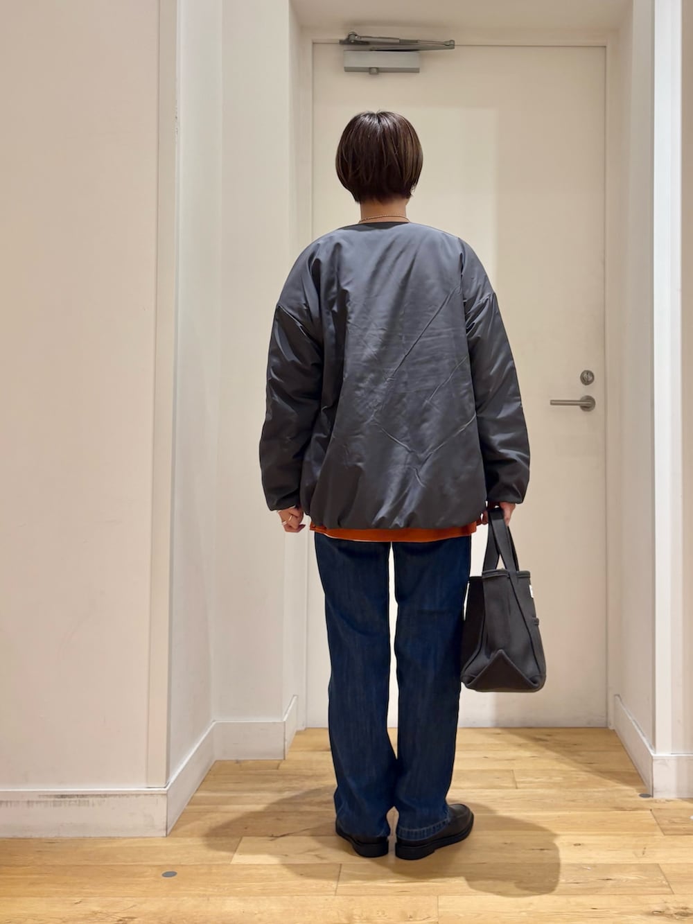 グレー系のブルゾン、オレンジ系のニット/セーター、ホワイト系のTシャツ/カットソーを着用したレディースの秋コーディネートの5枚目の写真