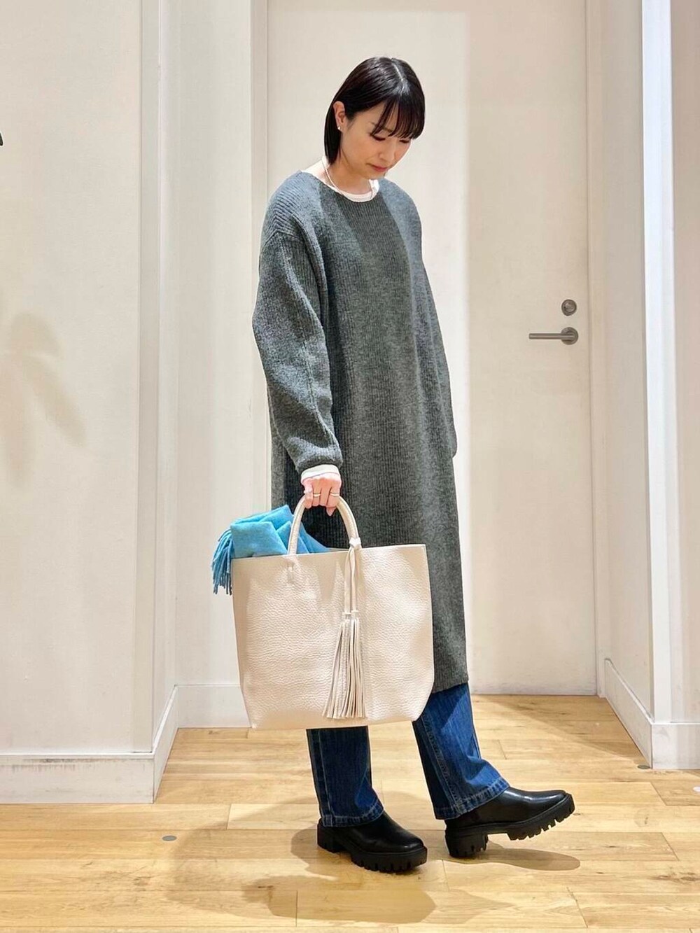 ホワイト系のトートバッグ、ブルー系のデニムパンツ、ブラック系のブーツを着用したレディースの冬コーディネートの4枚目の写真