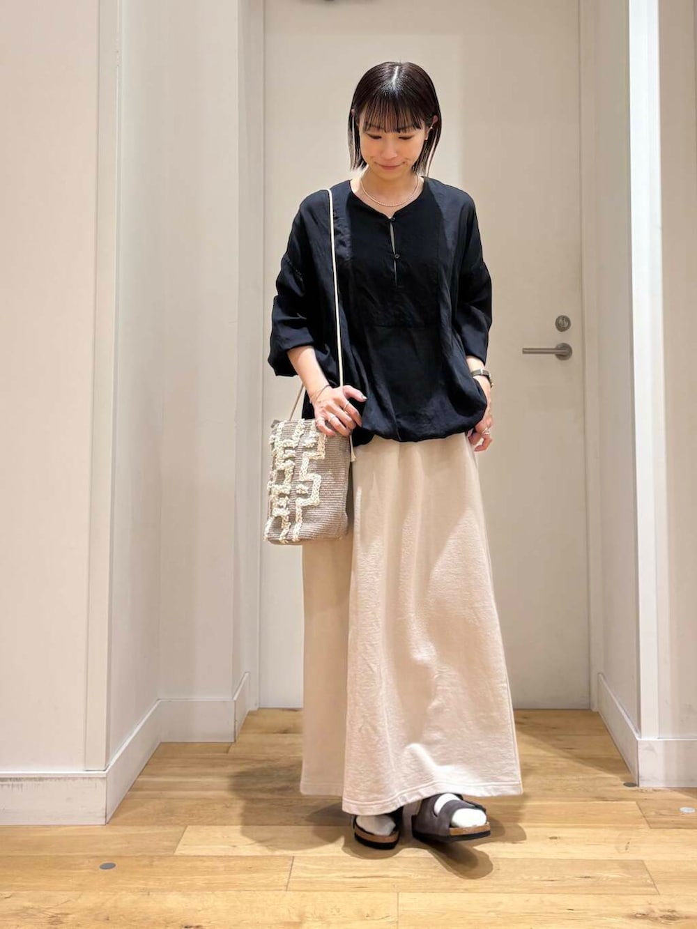 グレー系のショルダーバッグ、ブラック系のチュニック、グレー系のサンダルを着用したレディースの春コーディネートの2枚目の写真