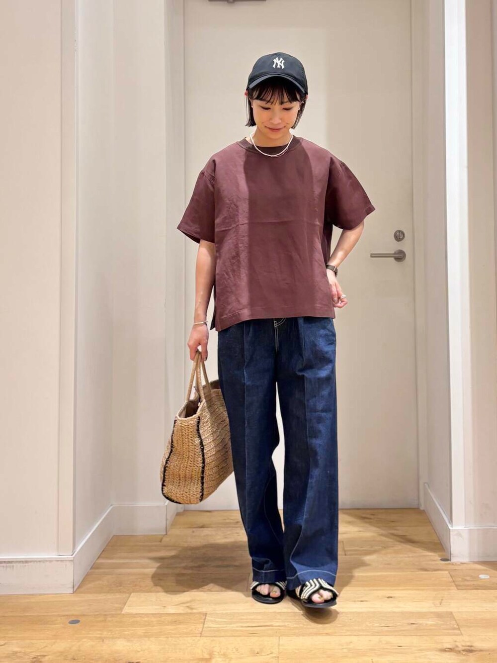 ベージュ系のトートバッグ、ブルー系のデニムパンツ、ブラック系のサンダルを着用したレディースの夏コーディネートの2枚目の写真