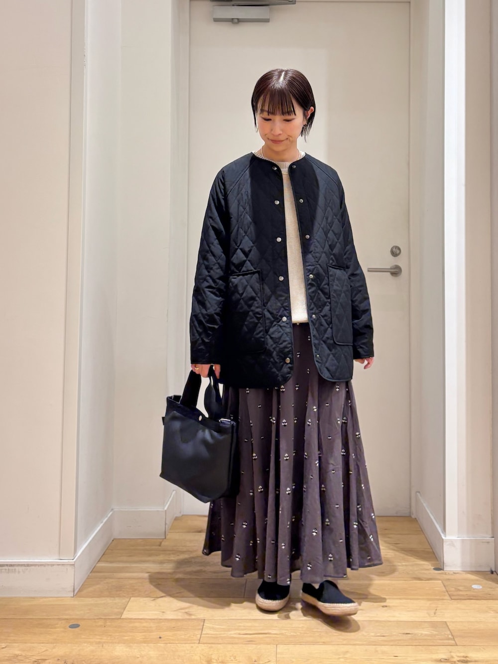 ブラック系のハンドバッグ、グレー系のニット/セーター、グレー系のスカートを着用したレディースの春コーディネートの2枚目の写真