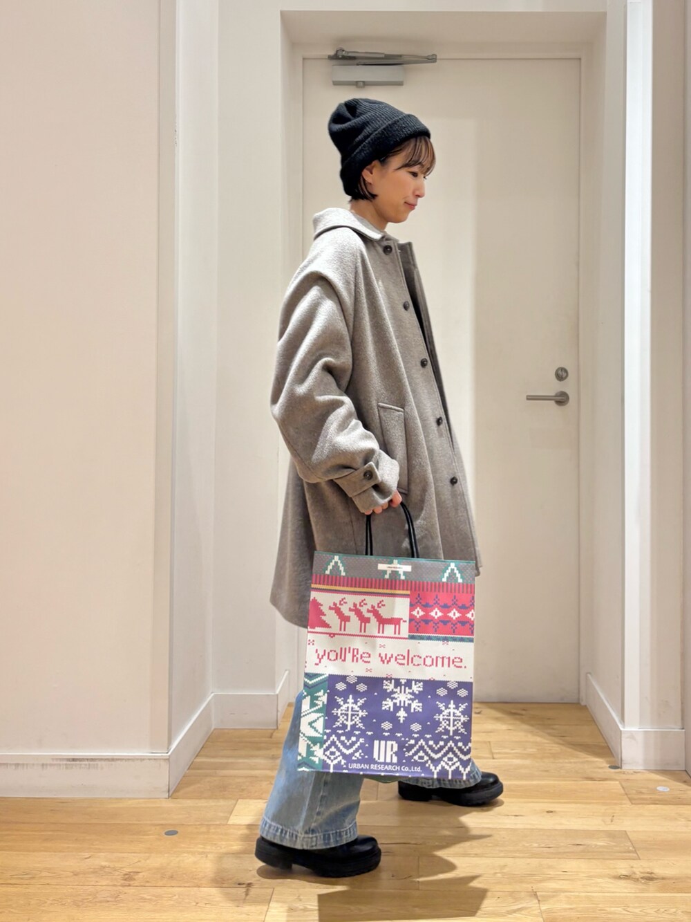 グレー系のステンカラーコート、ブルー系のデニムパンツ、ブラック系のブーツを着用したレディースの秋コーディネートの6枚目の写真