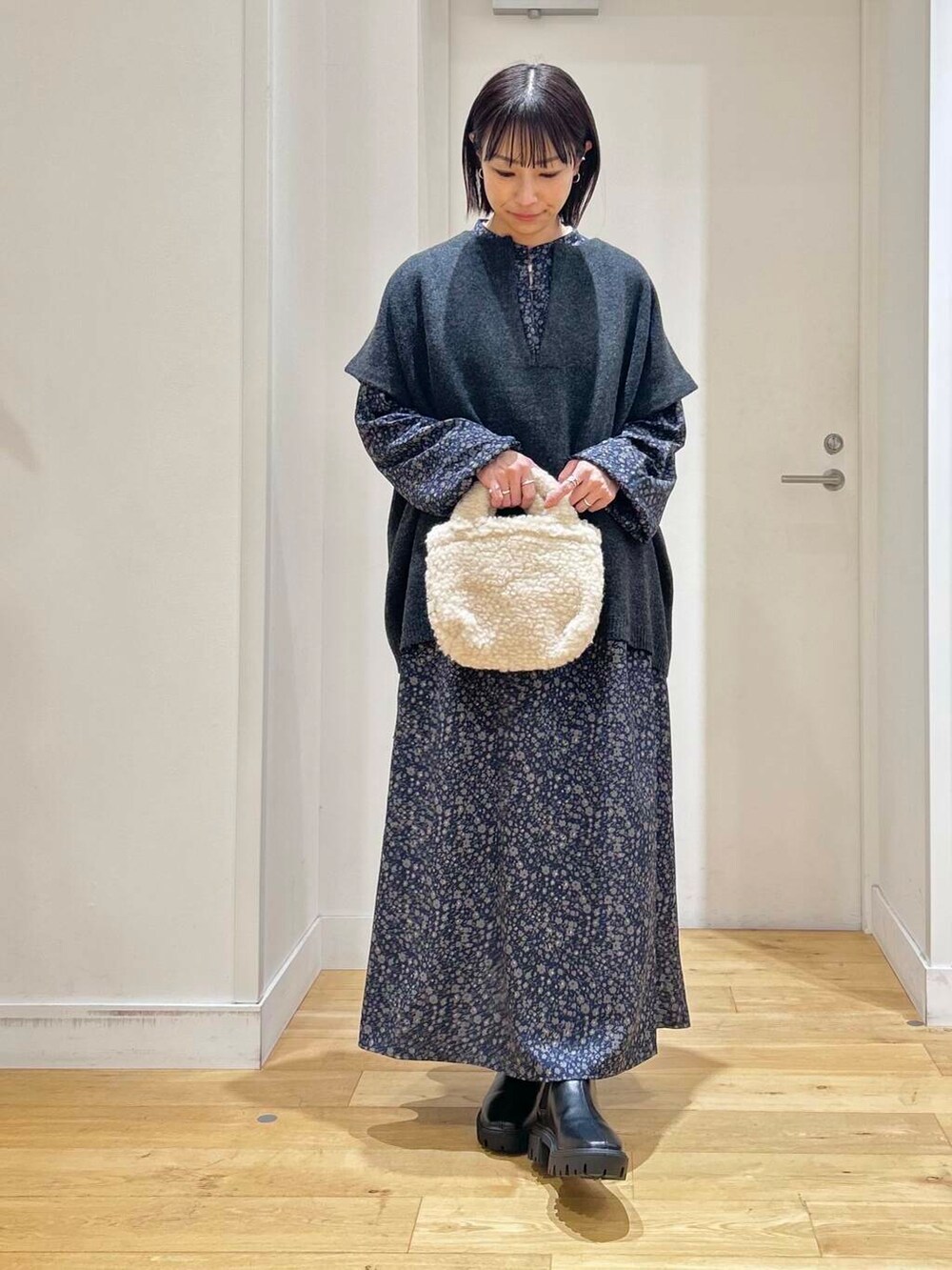 ブラック系のブーツ、ベージュ系のハンドバッグ、ブルー系のワンピースを着用したレディースの冬コーディネートの2枚目の写真