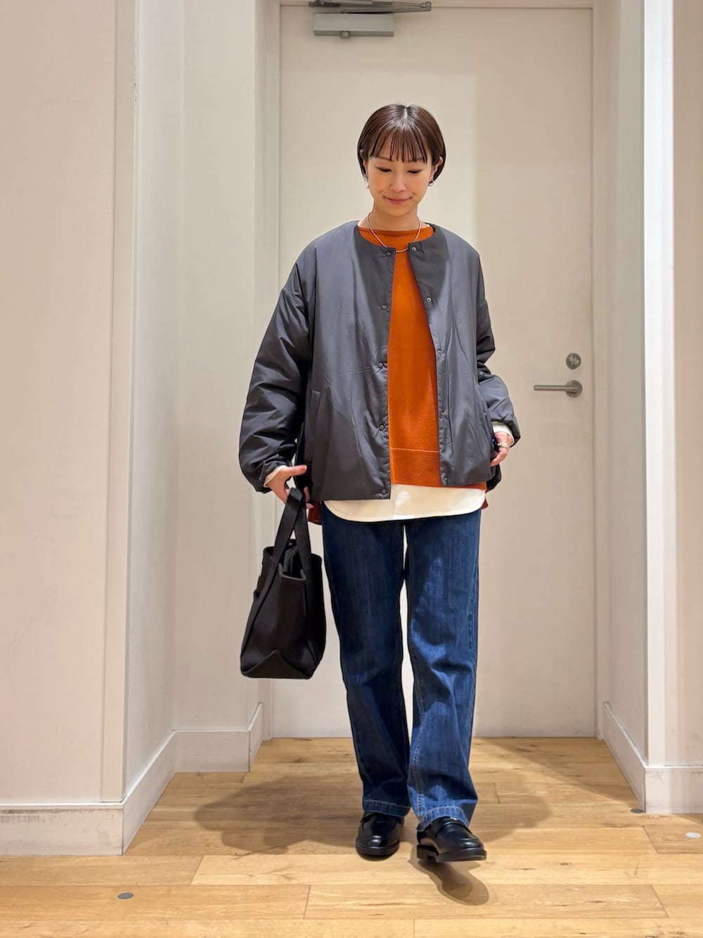 グレー系のブルゾン、オレンジ系のニット/セーター、ホワイト系のTシャツ/カットソーを着用したレディースの秋コーディネートの2枚目の写真