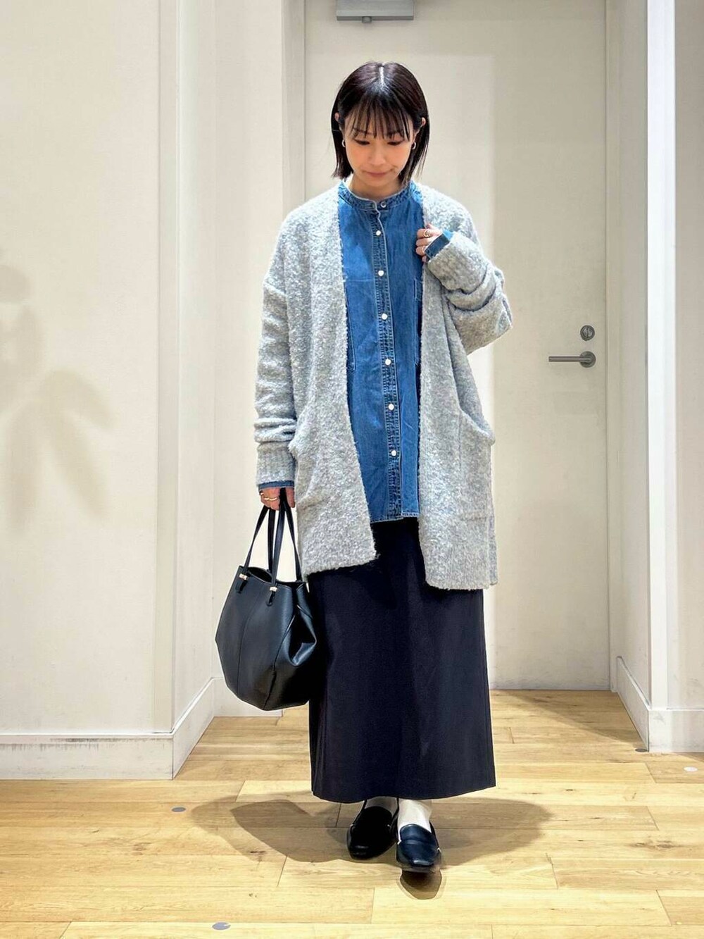ブラック系のローファー、ブラック系のショルダーバッグ、ブルー系のスカートを着用したレディースの秋コーディネートの2枚目の写真