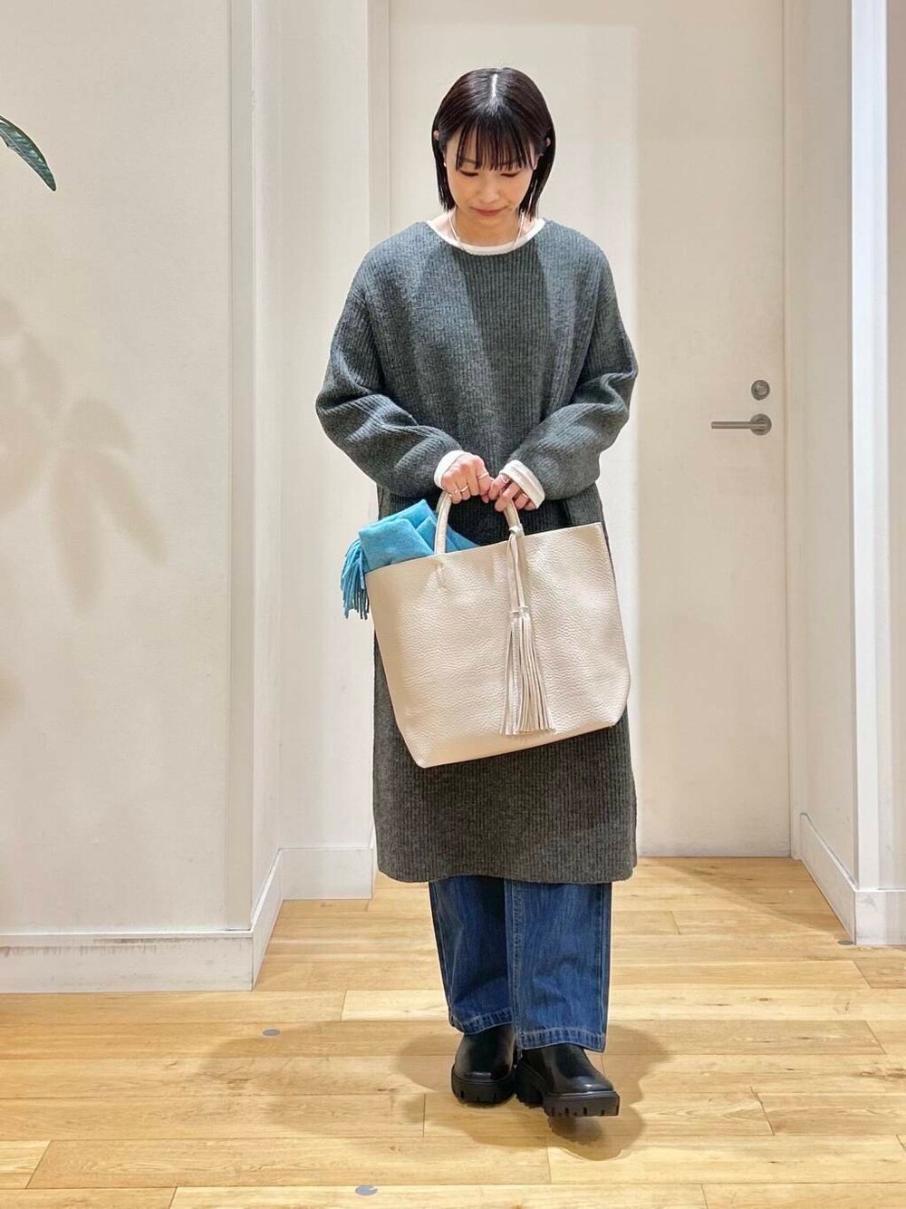 ホワイト系のトートバッグ、ブルー系のデニムパンツ、ブラック系のブーツを着用したレディースの冬コーディネートの3枚目の写真