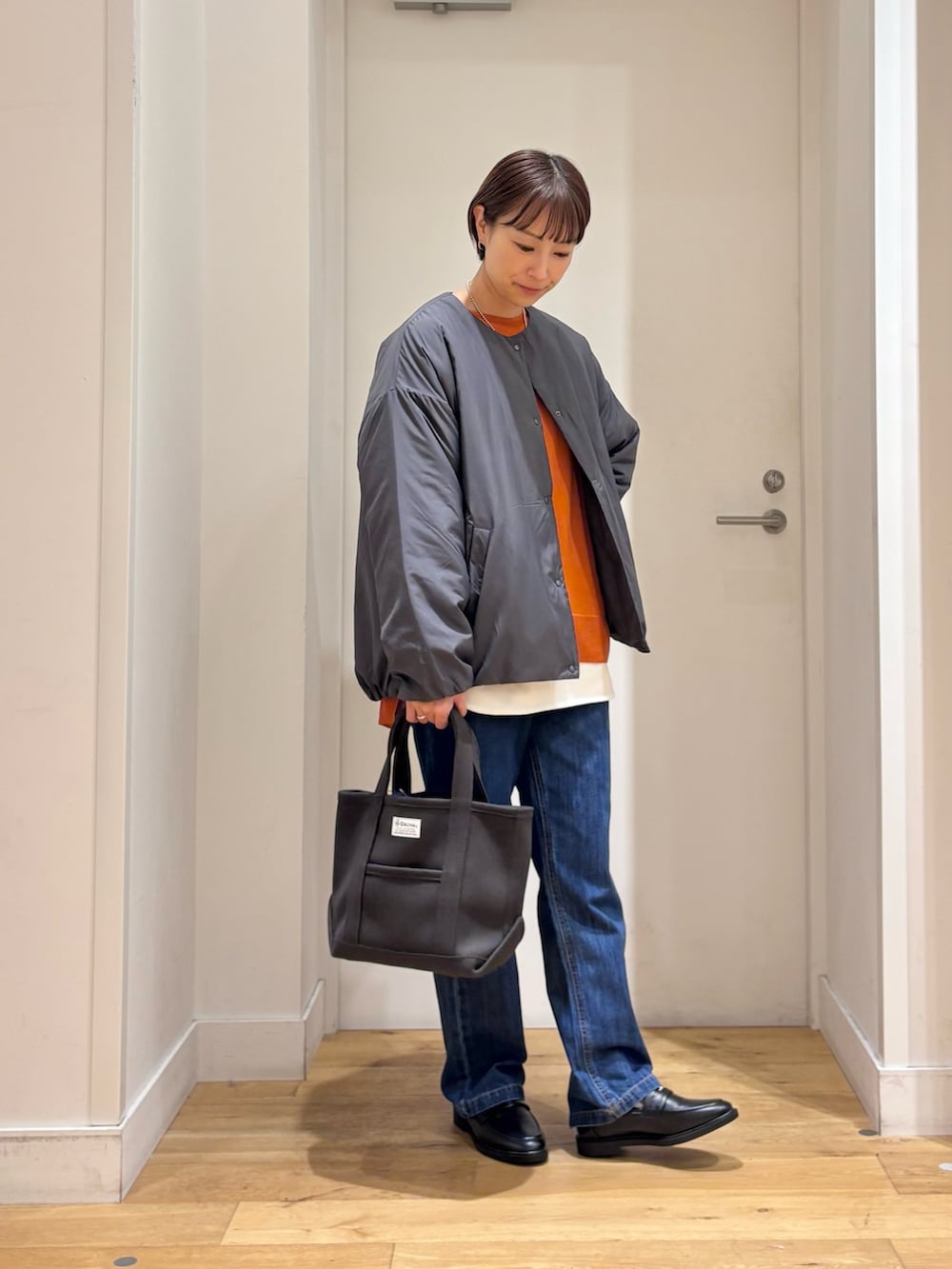 グレー系のブルゾン、オレンジ系のニット/セーター、ホワイト系のTシャツ/カットソーを着用したレディースの秋コーディネートの4枚目の写真