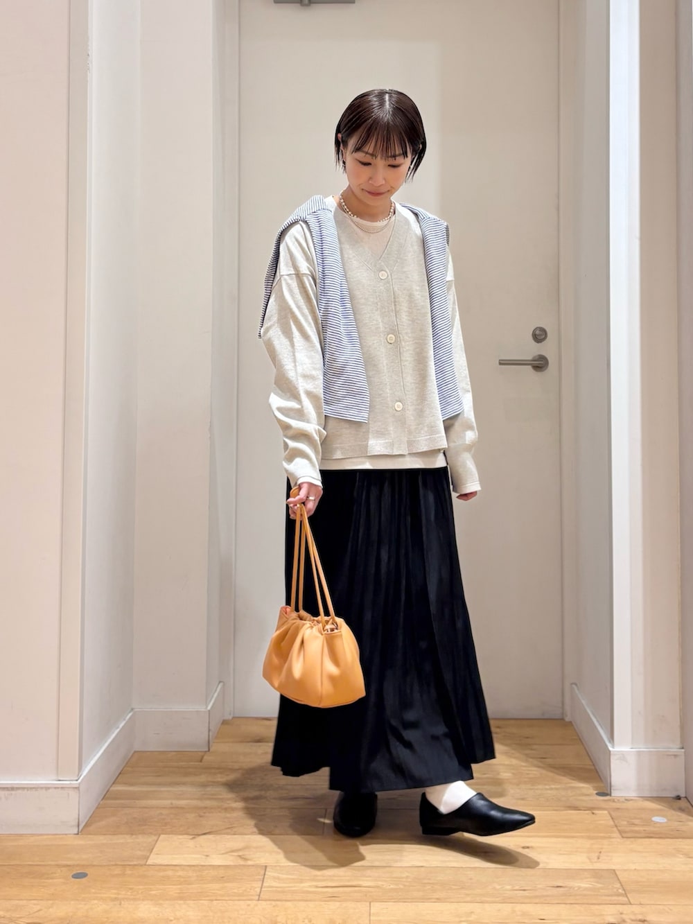 ベージュ系のTシャツ/カットソー、ベージュ系のカーディガン/ボレロ、ブラック系のスカートを着用したレディースの春コーディネートの4枚目の写真