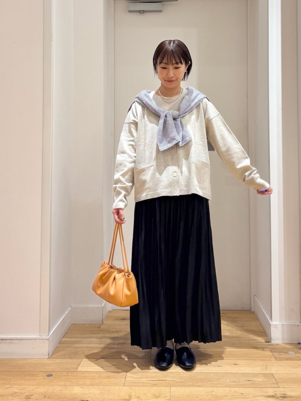 ベージュ系のTシャツ/カットソー、ベージュ系のカーディガン/ボレロ、ブラック系のスカートを着用したレディースの春コーディネートの2枚目の写真