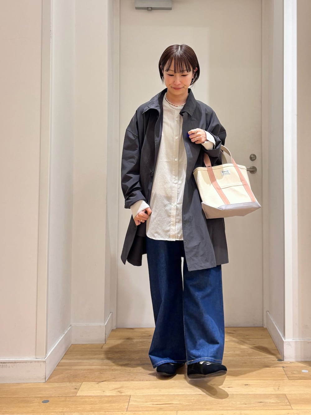 グレー系のステンカラーコート、グレー系のシャツ/ブラウス、ブルー系のデニムパンツを着用したレディースの春コーディネートの2枚目の写真