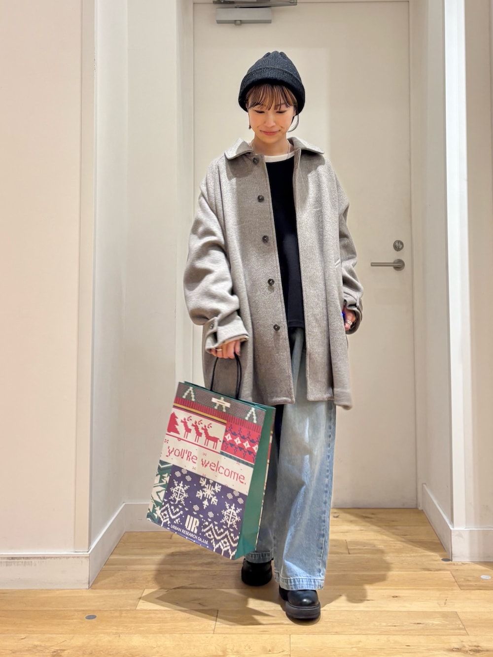 グレー系のステンカラーコート、ブルー系のデニムパンツ、ブラック系のブーツを着用したレディースの秋コーディネートの2枚目の写真