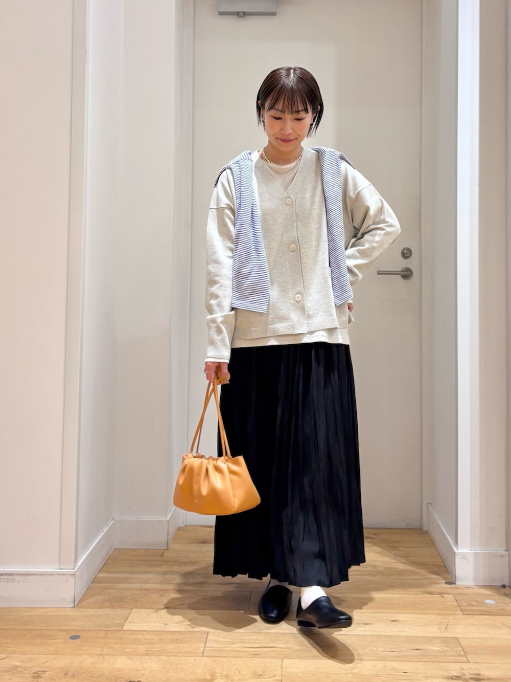 ベージュ系のTシャツ/カットソー、ベージュ系のカーディガン/ボレロ、ブラック系のスカートを着用したレディースの春コーディネートの5枚目の写真