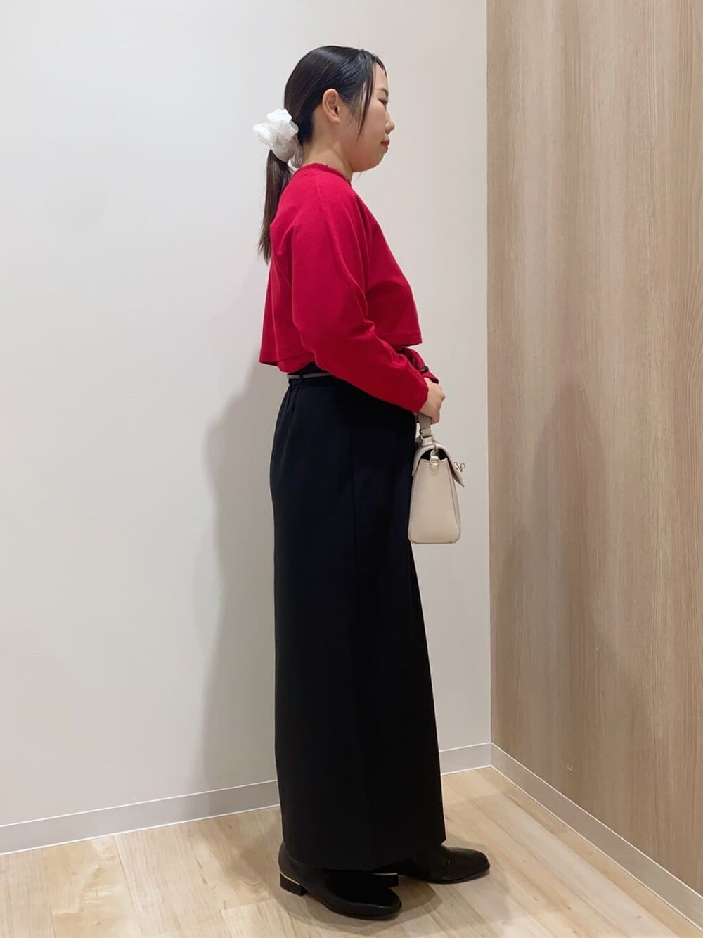 レッド系のアンサンブル、ブラック系のスカート、ベージュ系のショルダーバッグを着用したレディースの冬コーディネートの2枚目の写真