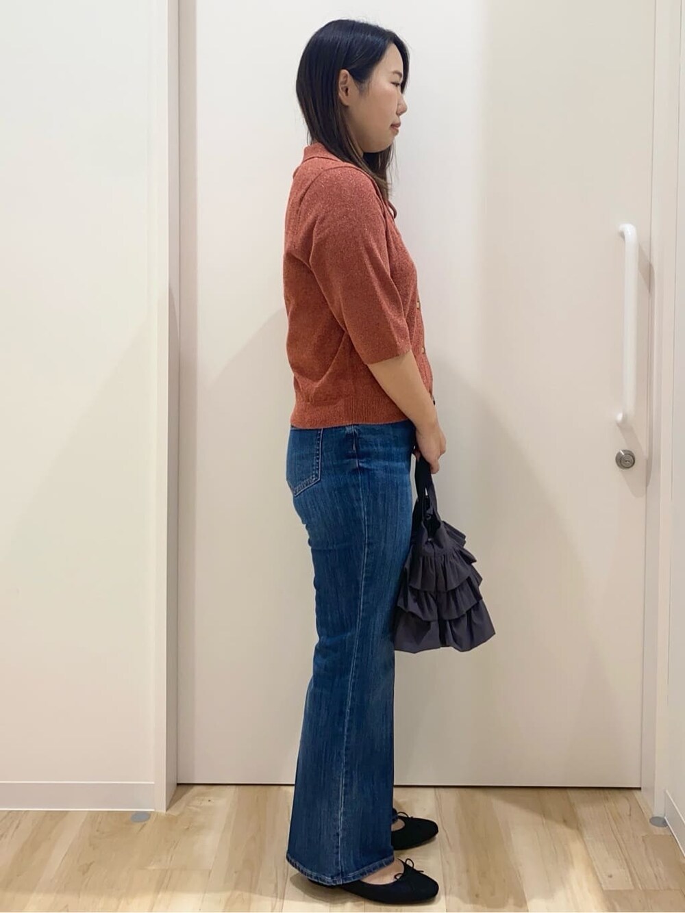 レッド系のニット/セーター、ブルー系のデニムパンツ、グレー系のトートバッグを着用したレディースの秋コーディネートの2枚目の写真