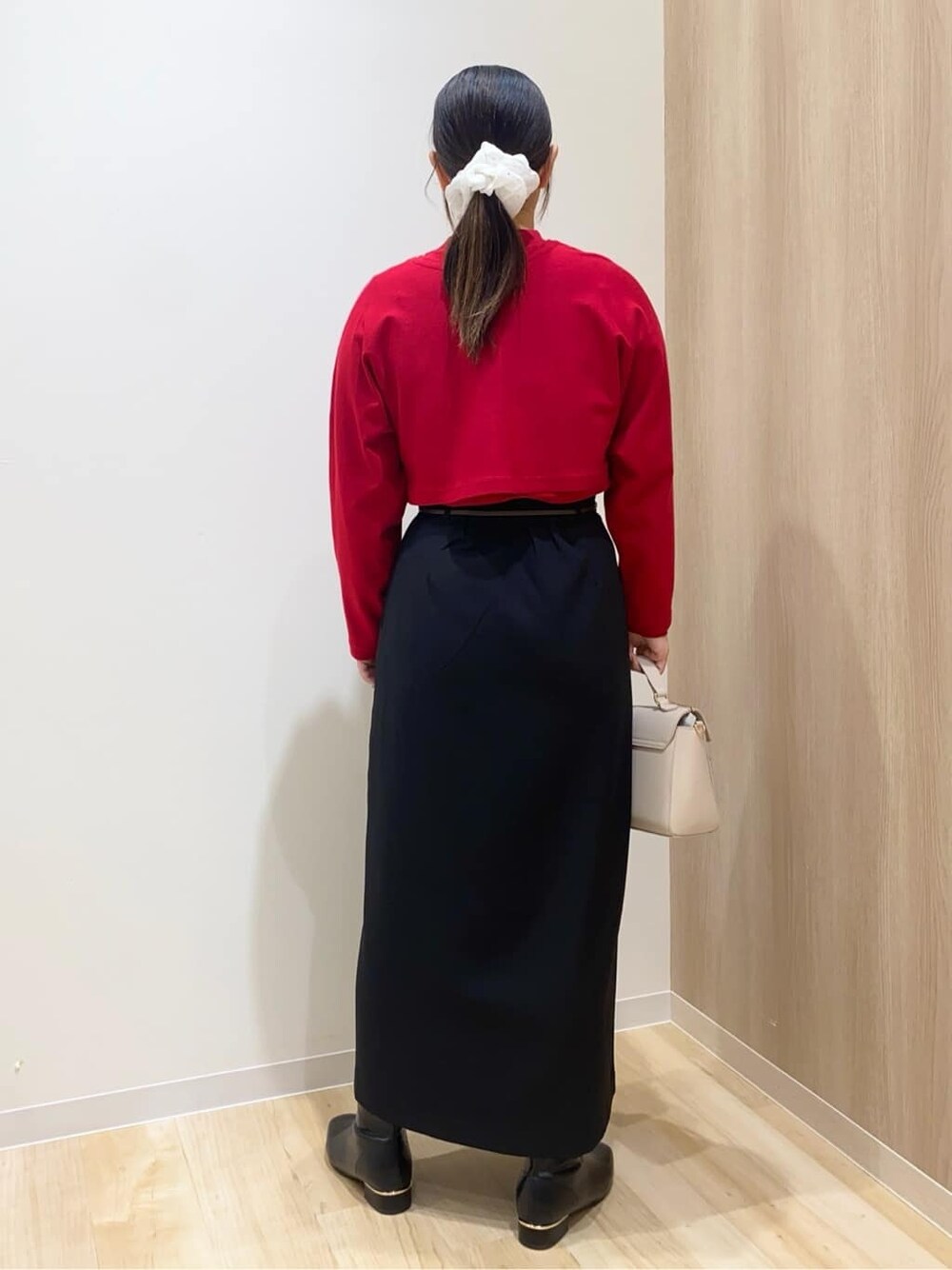 レッド系のアンサンブル、ブラック系のスカート、ベージュ系のショルダーバッグを着用したレディースの冬コーディネートの3枚目の写真