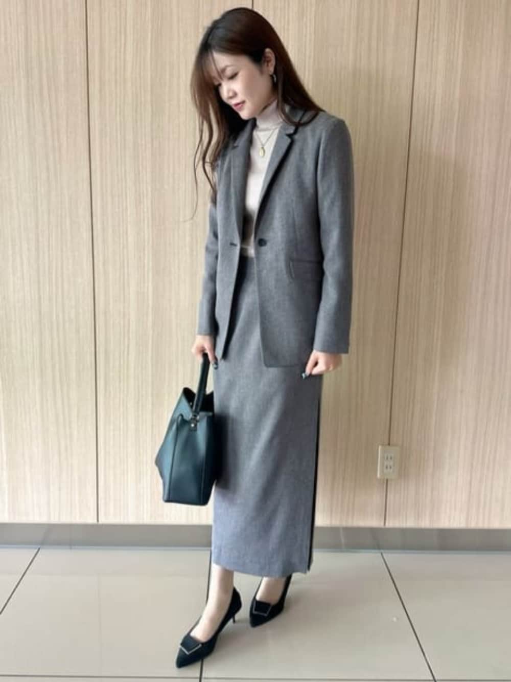 グレー系のスカート、グレー系のテーラードジャケット、ブラック系のショルダーバッグを着用したレディースの冬コーディネートの2枚目の写真