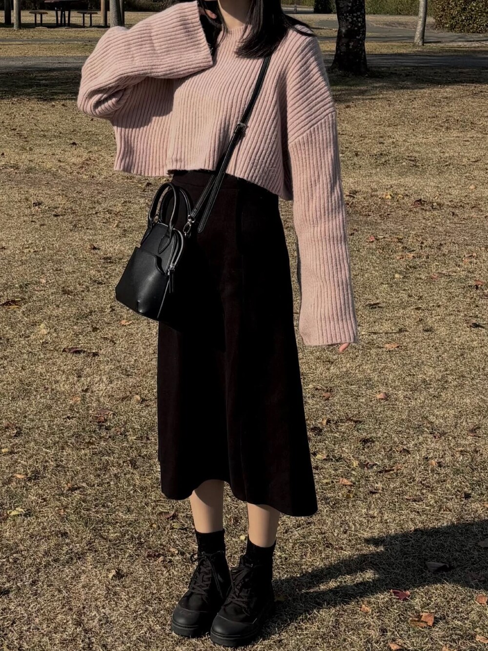 ブラック系のスカート、ピンク系のニット/セーター、ブラック系のブーティを着用したレディースの冬コーディネートの2枚目の写真