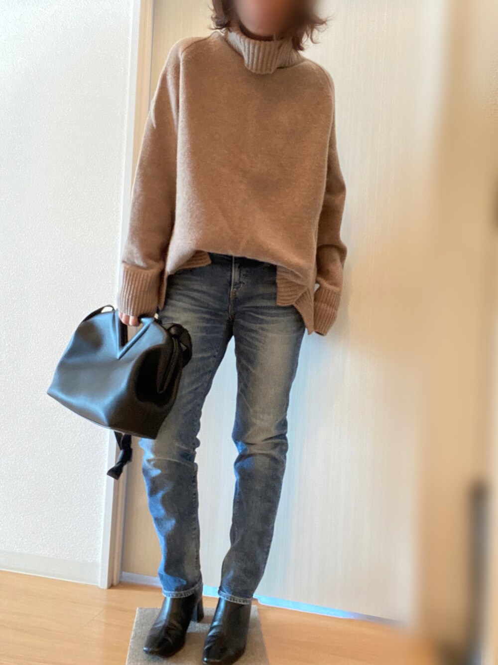 ブラック系のステンカラーコート、ベージュ系のニット/セーター、ブルー系のデニムパンツを着用したレディースの冬コーディネートの2枚目の写真