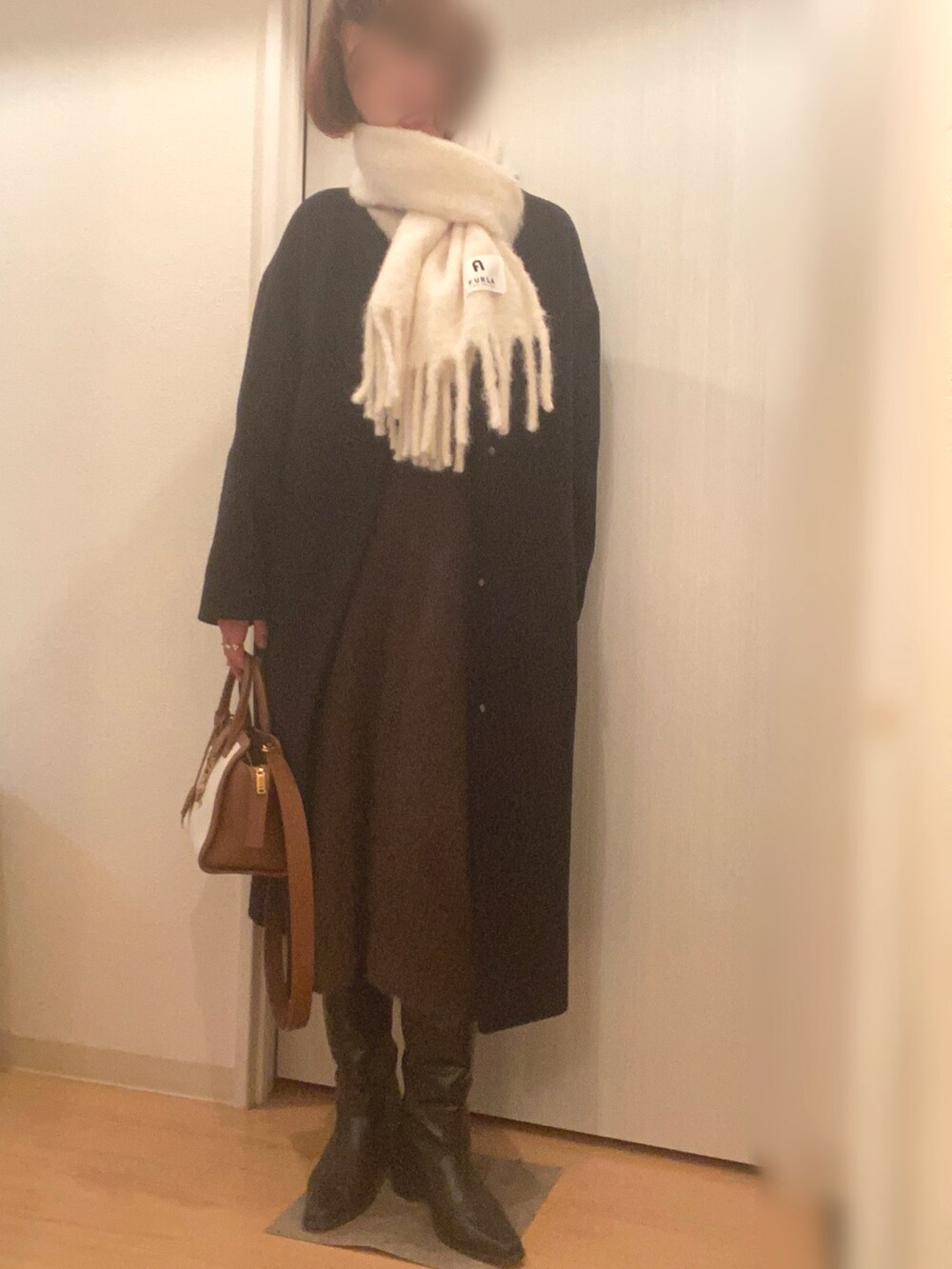 ブラック系のステンカラーコート、グリーン系のワンピース、ブラック系のブーツを着用したレディースの冬コーディネートの3枚目の写真