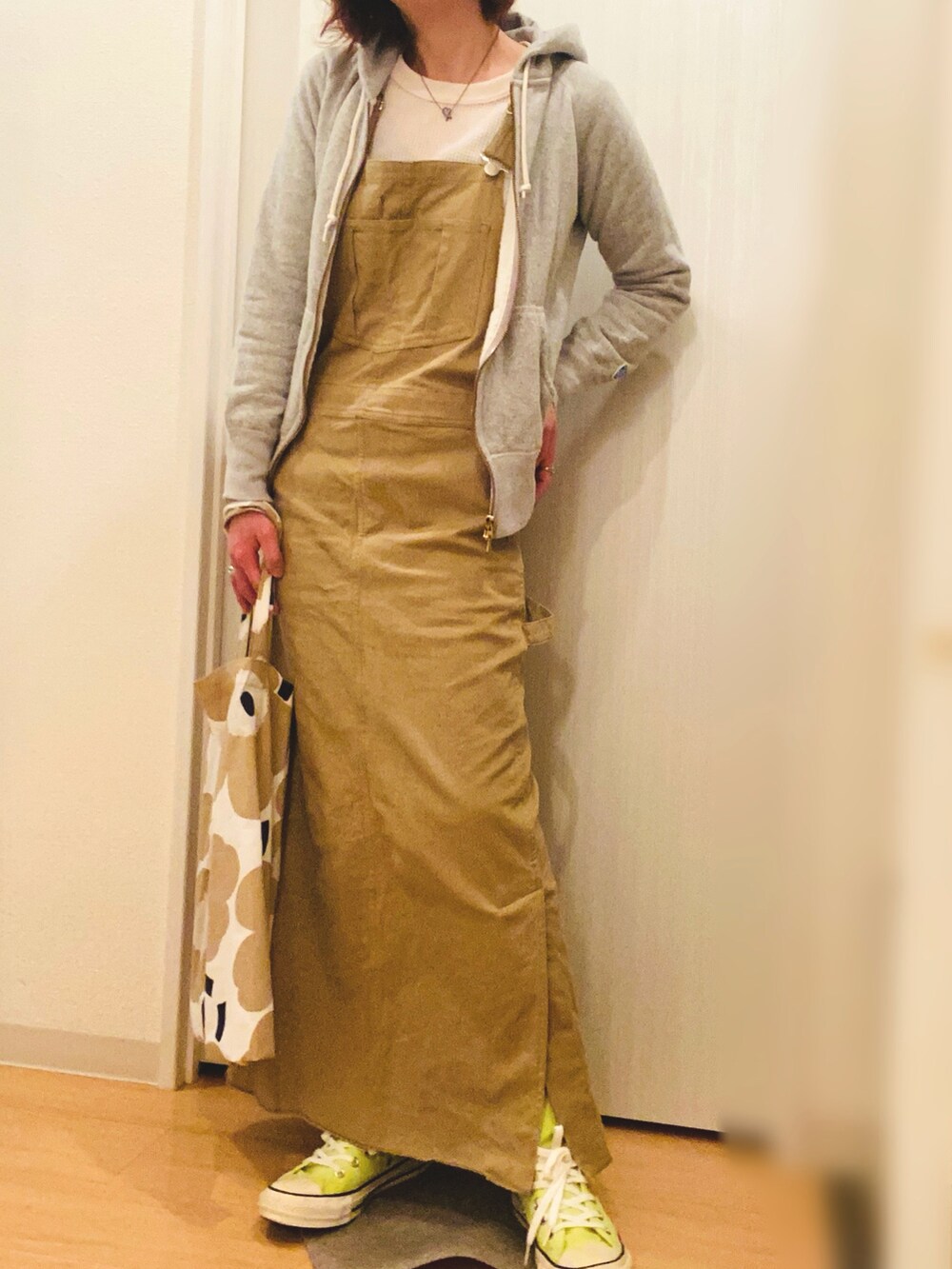 グレー系のパーカー、ベージュ系のジャンパースカート、イエロー系のスニーカーを着用したレディースの春コーディネートの2枚目の写真