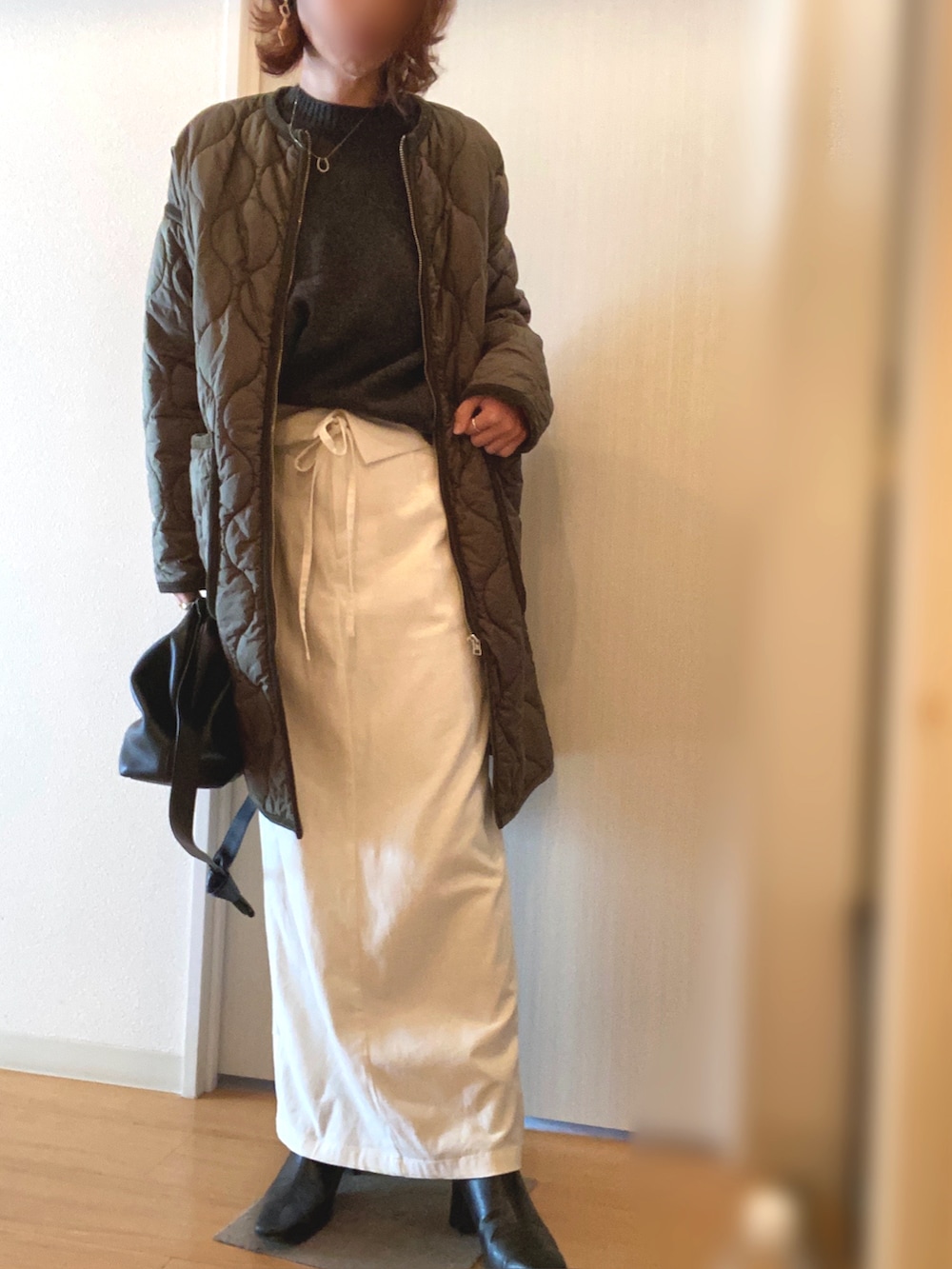 グリーン系のノーカラーコート、グレー系のニット/セーター、ホワイト系のスカートを着用したレディースの冬コーディネートの2枚目の写真