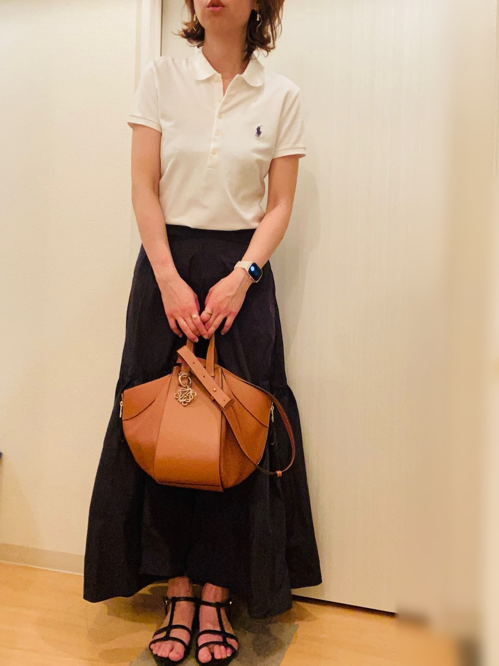 ホワイト系のポロシャツ、ブラック系のスカート、ブラック系のサンダルを着用したレディースの夏コーディネートの2枚目の写真