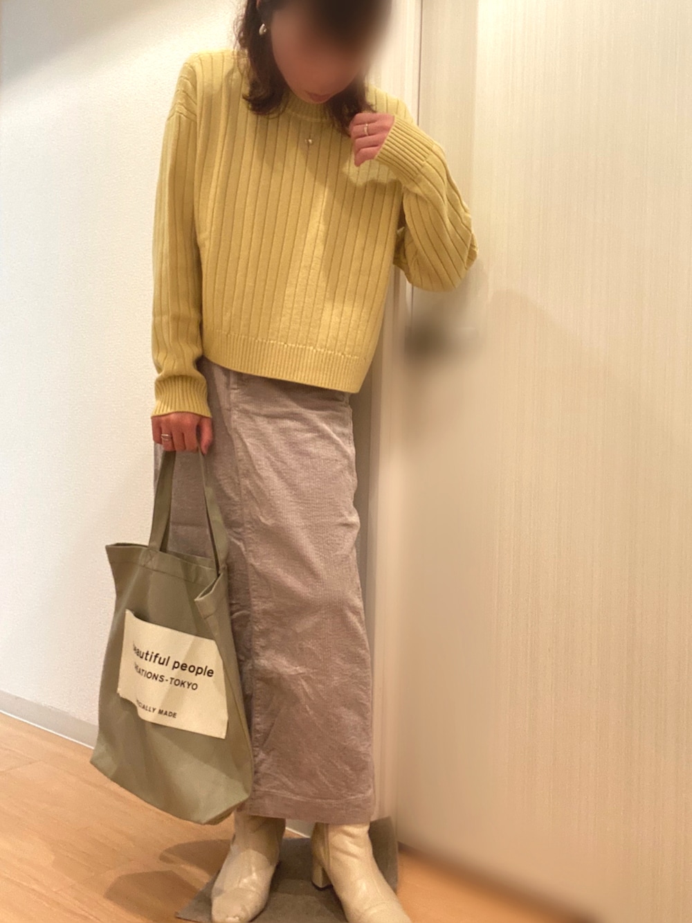 イエロー系のニット/セーター、グレー系のスカート、ベージュ系のブーツを着用したレディースの春コーディネートの2枚目の写真