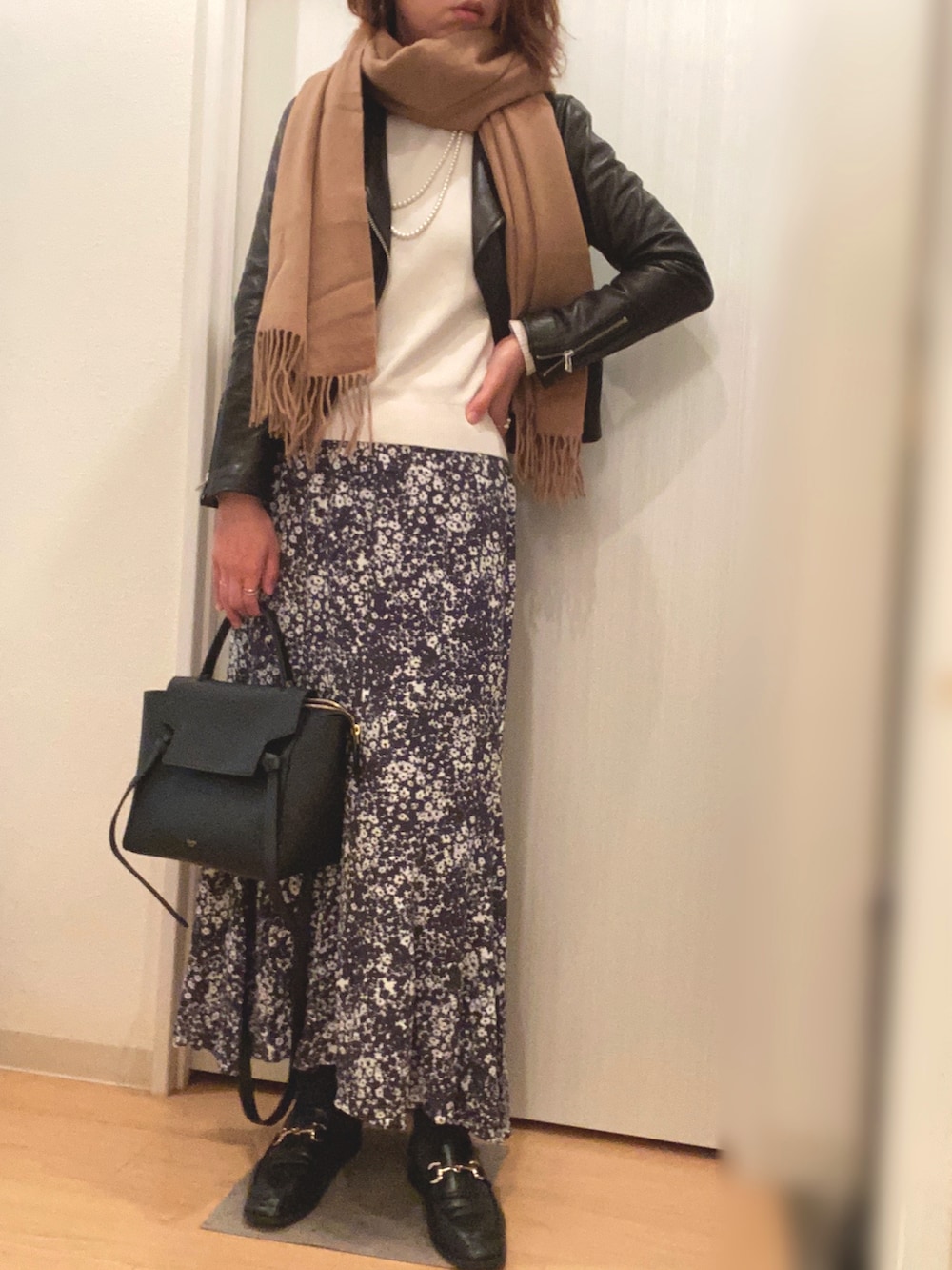 ブラック系のライダースジャケット、ホワイト系のニット/セーター、グレー系のスカートを着用したレディースの秋コーディネートの2枚目の写真