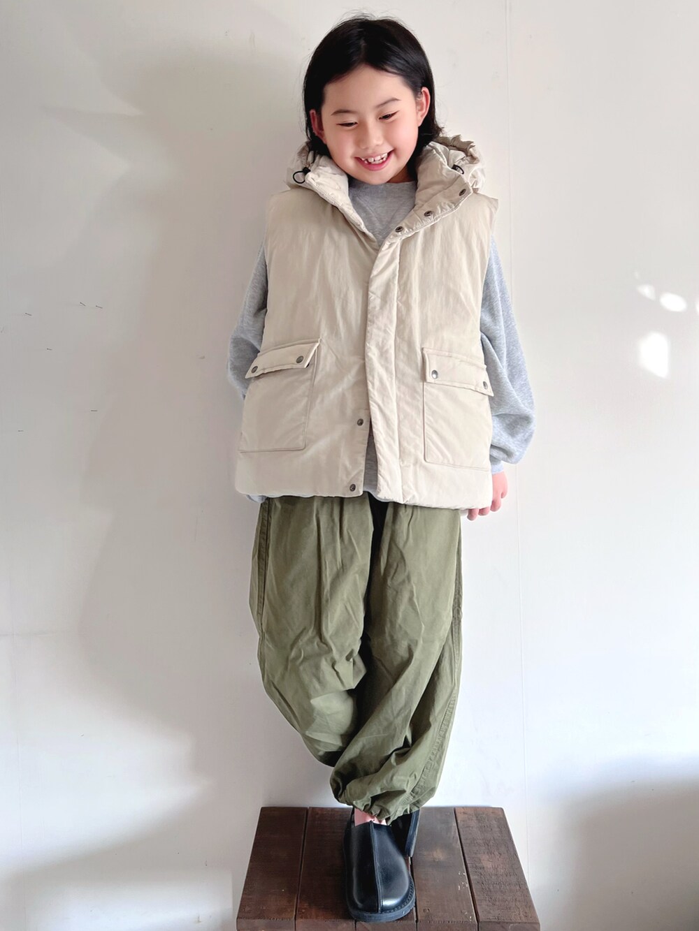 ホワイト系のダウンベスト、グレー系のスウェット、グリーン系のその他パンツを着用したキッズの冬コーディネートの2枚目の写真