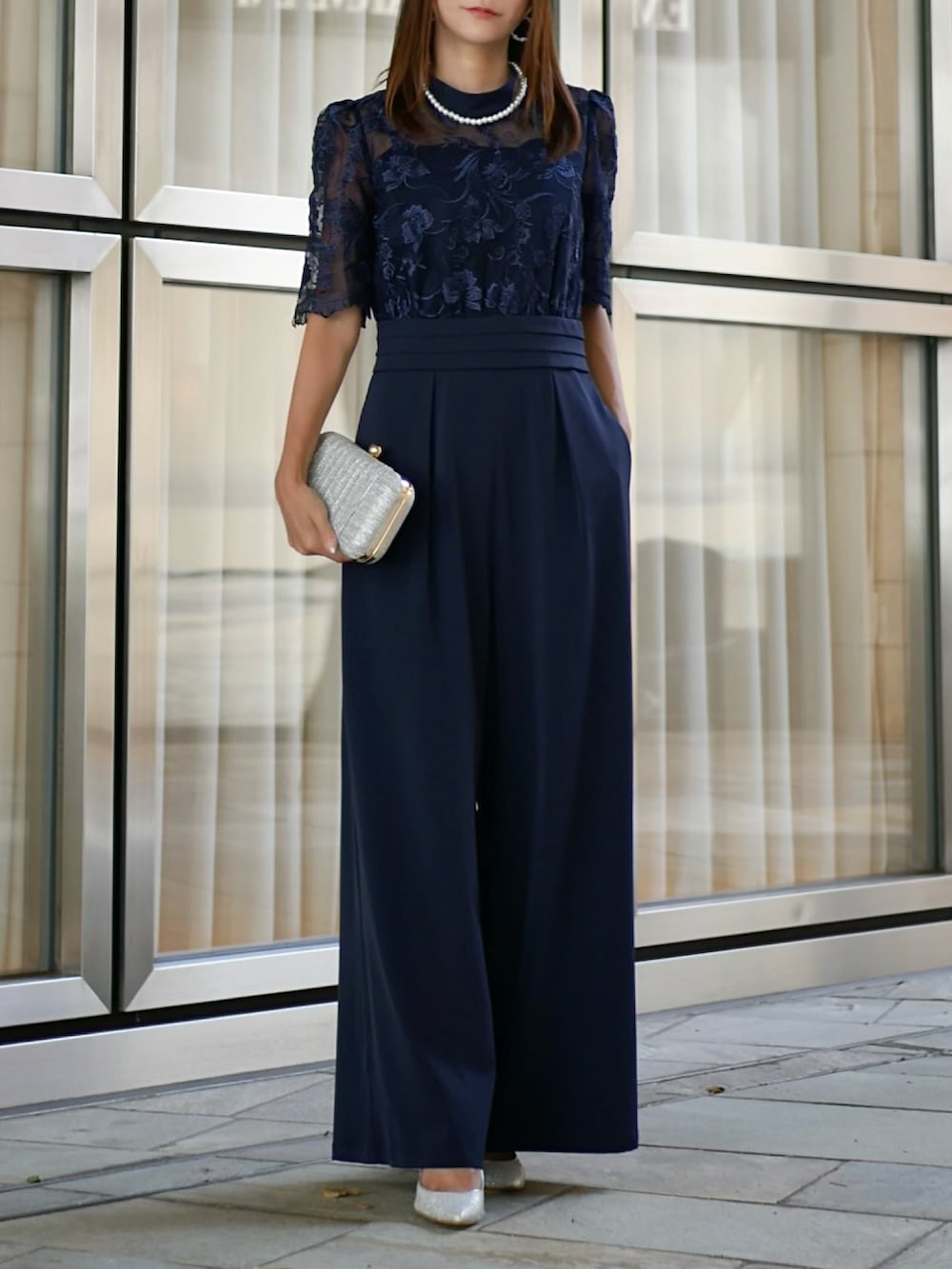 シルバー系のクラッチバッグ、ブルー系のパンツドレスを着用したレディースの夏コーディネートの2枚目の写真