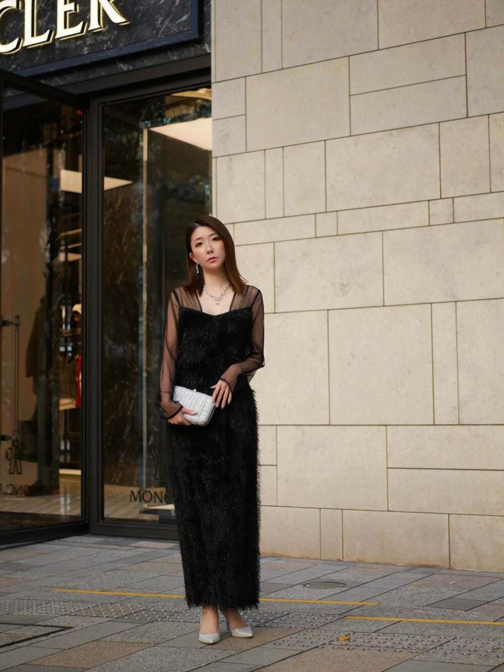 シルバー系のクラッチバッグ、ブラック系のドレスを着用したレディースの冬コーディネートの2枚目の写真