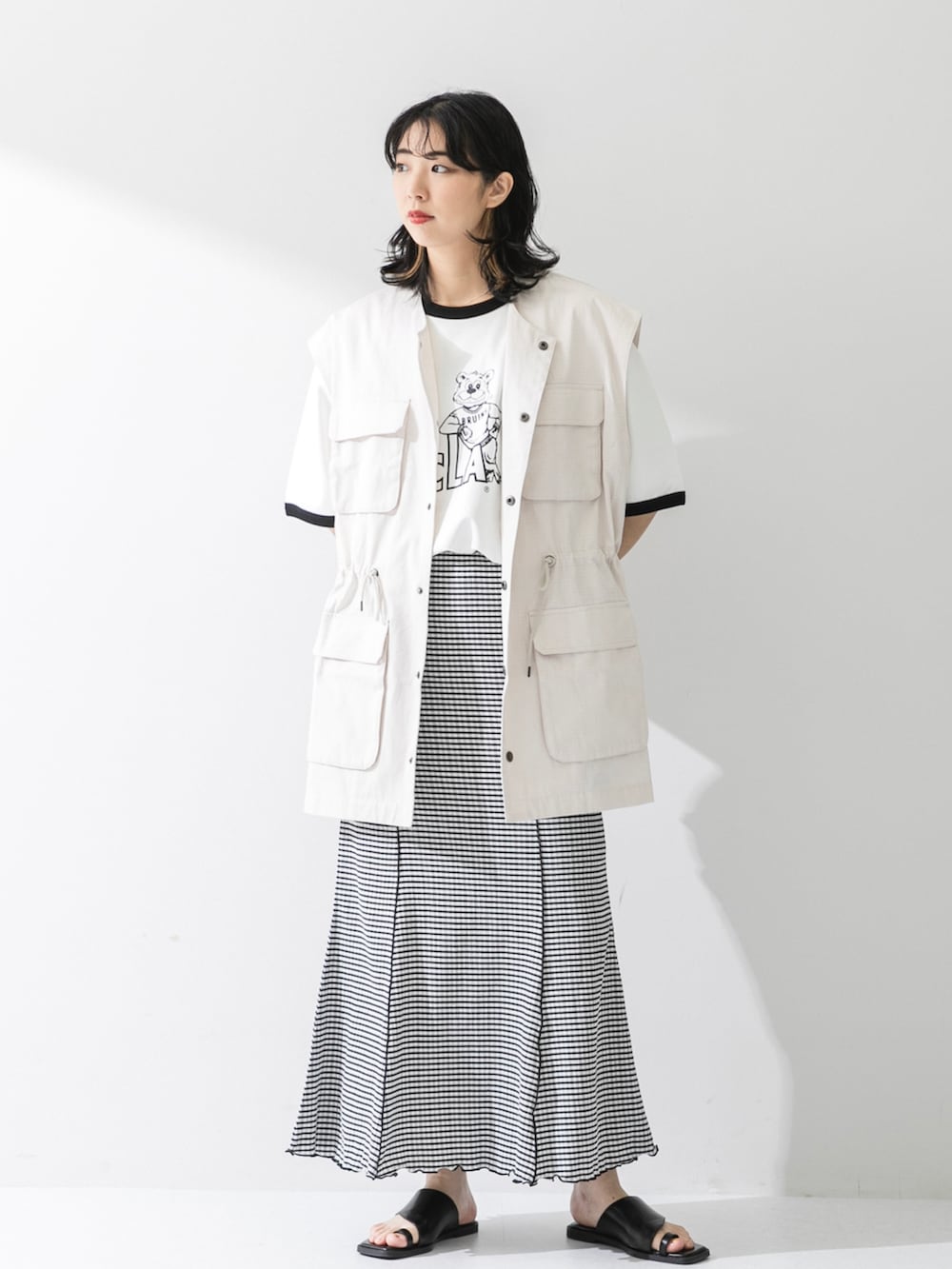 ブラック系のスカート、ホワイト系のTシャツ/カットソー、ブラック系のサンダルを着用したレディースの夏コーディネートの2枚目の写真