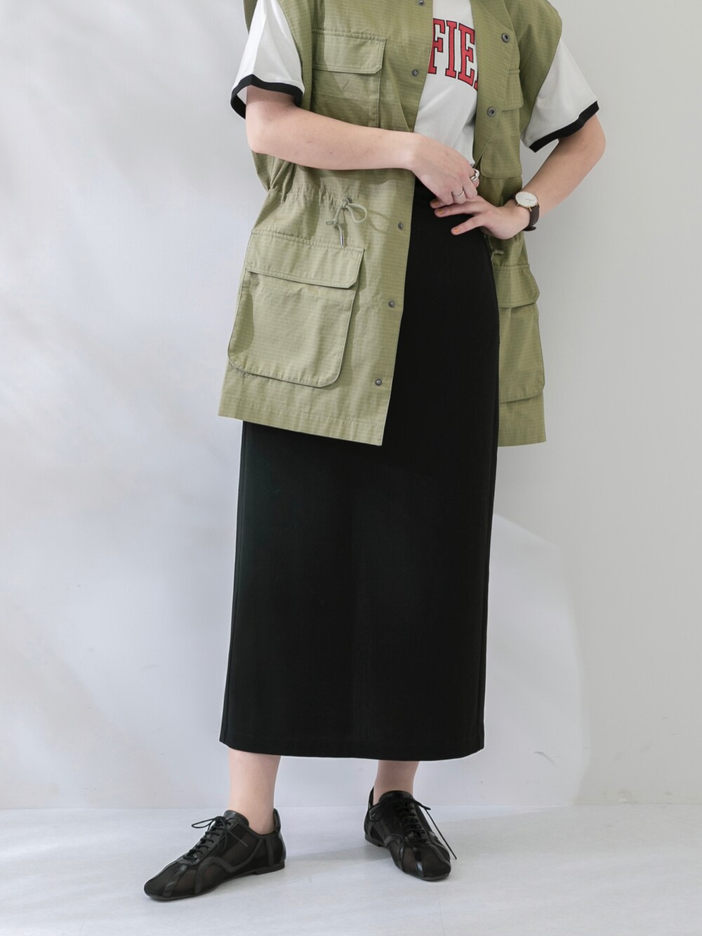 グリーン系のベスト、ホワイト系のTシャツ/カットソー、ブラック系のスカートを着用したレディースの春コーディネートの5枚目の写真