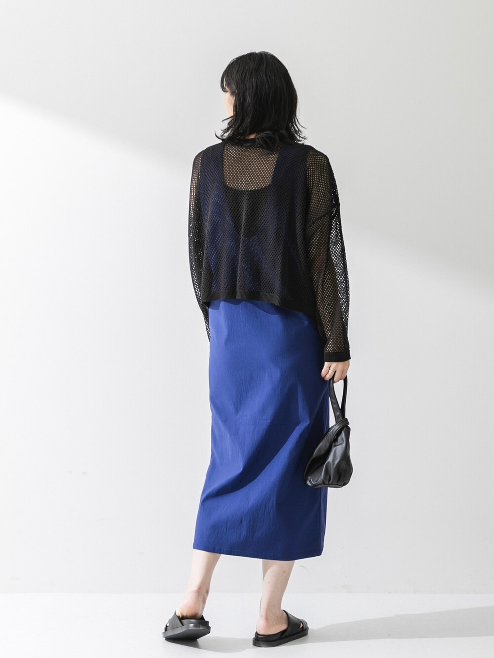 ブラック系のカーディガン/ボレロ、ブルー系のジャンパースカート、ブラック系のハンドバッグを着用したレディースの夏コーディネートの2枚目の写真