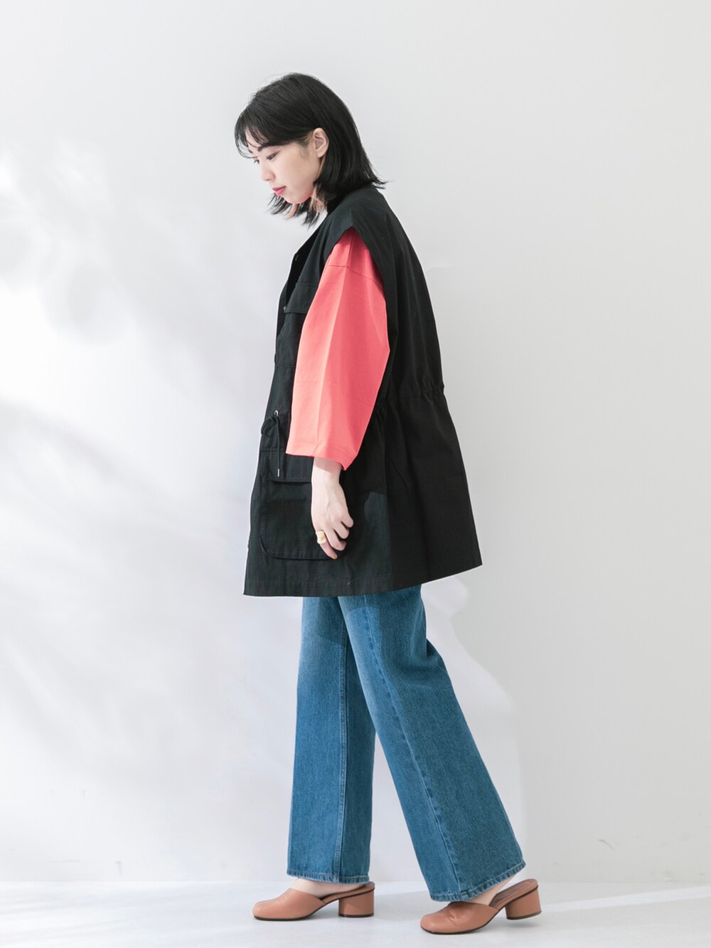 ブラック系のベスト、オレンジ系のTシャツ/カットソー、ブルー系のデニムパンツを着用したレディースの春コーディネートの2枚目の写真