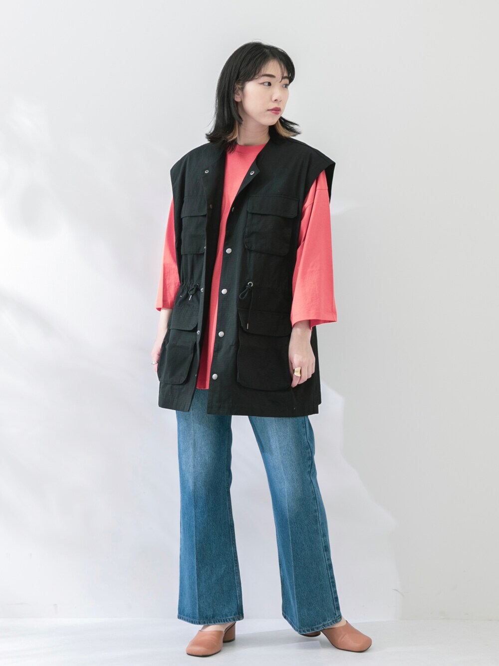 ブラック系のベスト、オレンジ系のTシャツ/カットソー、ブルー系のデニムパンツを着用したレディースの春コーディネートの3枚目の写真