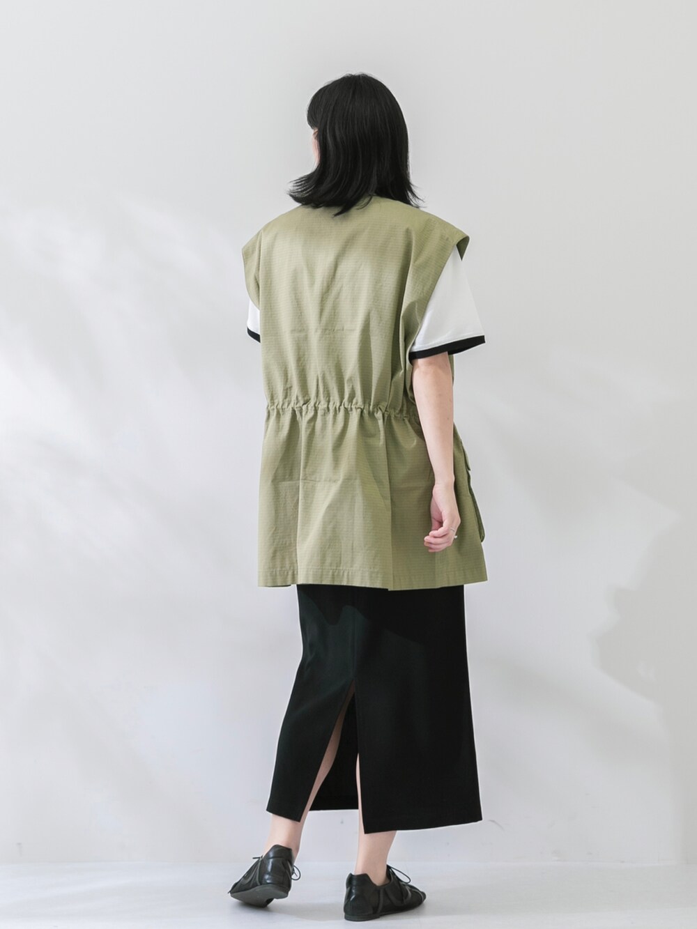 グリーン系のベスト、ホワイト系のTシャツ/カットソー、ブラック系のスカートを着用したレディースの春コーディネートの3枚目の写真