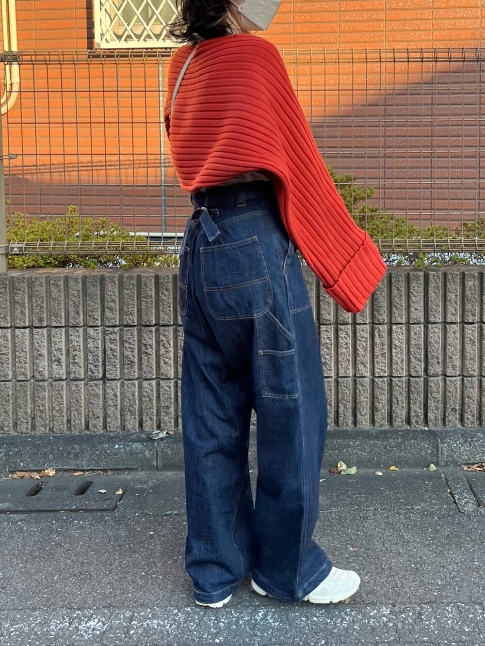 レッド系のニット/セーター、ブルー系のデニムパンツ、ベージュ系のボディバッグ/ウエストポーチを着用したレディースの秋コーディネートの2枚目の写真