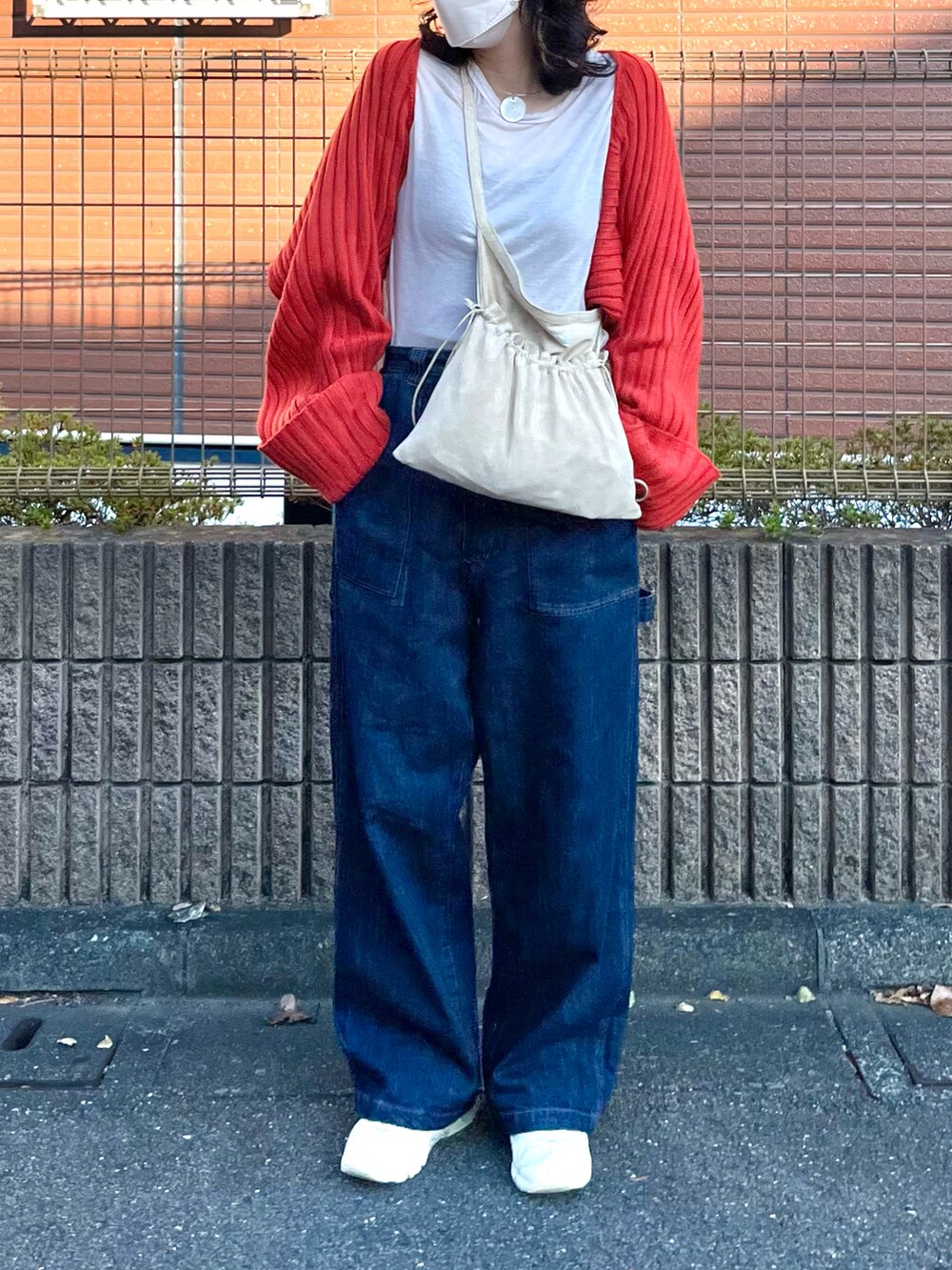 レッド系のニット/セーター、ブルー系のデニムパンツ、ベージュ系のボディバッグ/ウエストポーチを着用したレディースの秋コーディネートの3枚目の写真