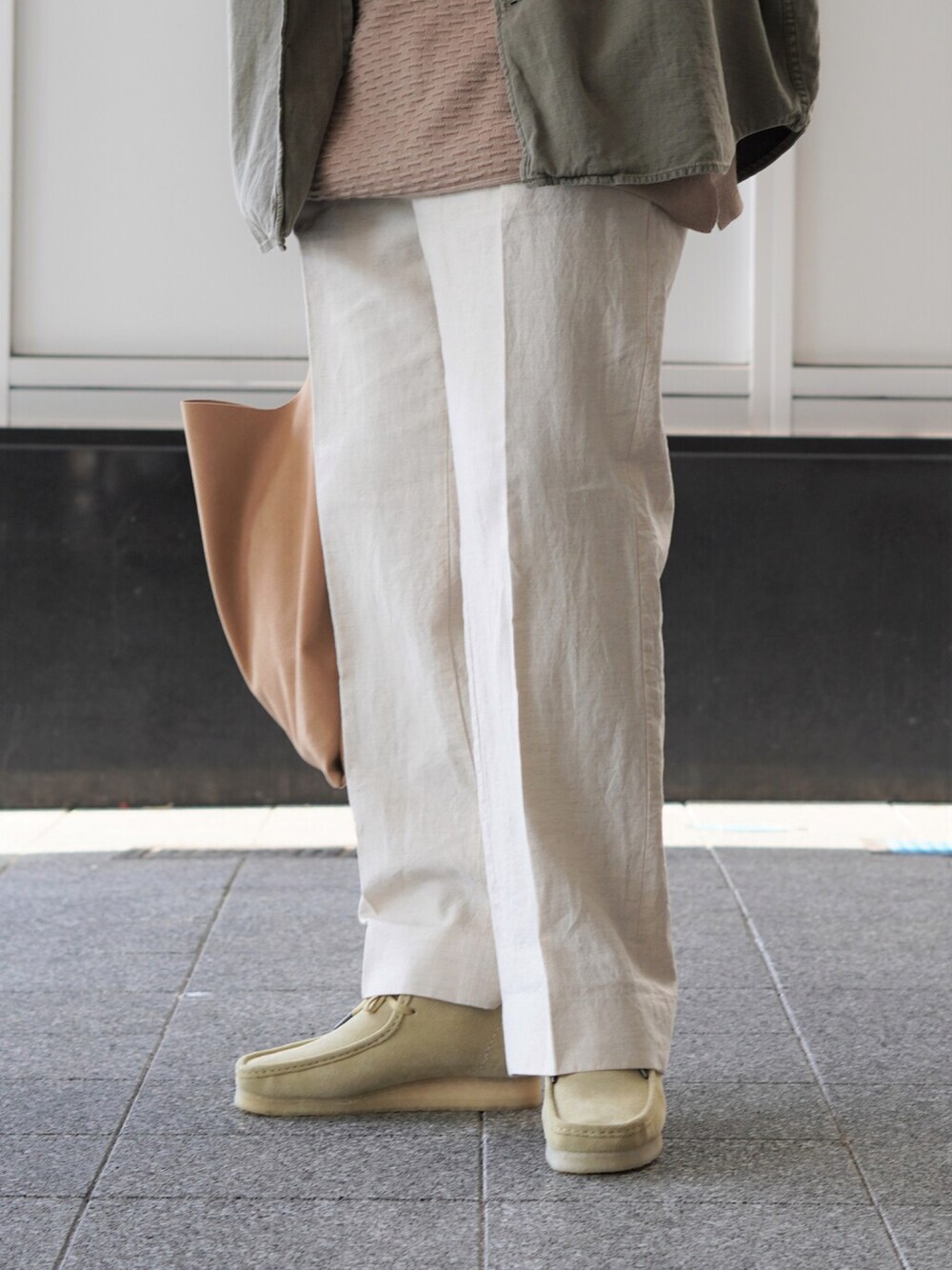 ブラウン系のトートバッグ、ベージュ系のTシャツ/カットソー、ベージュ系のスラックスを着用したメンズの春コーディネートの3枚目の写真