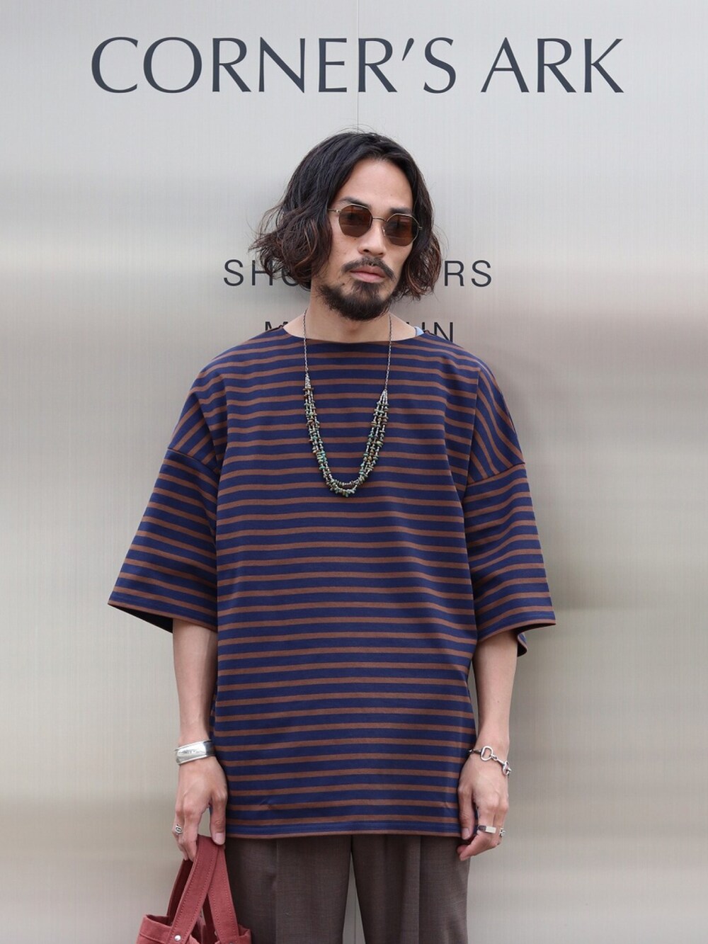 ブルー系のTシャツ/カットソー、ブラウン系のスラックス、レッド系のトートバッグを着用したメンズの夏コーディネートの2枚目の写真