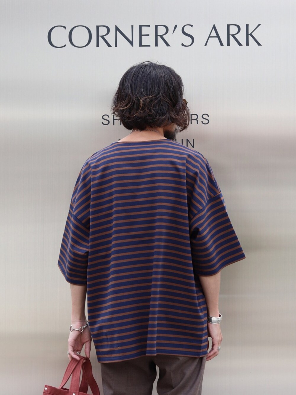 ブルー系のTシャツ/カットソー、ブラウン系のスラックス、レッド系のトートバッグを着用したメンズの夏コーディネートの3枚目の写真