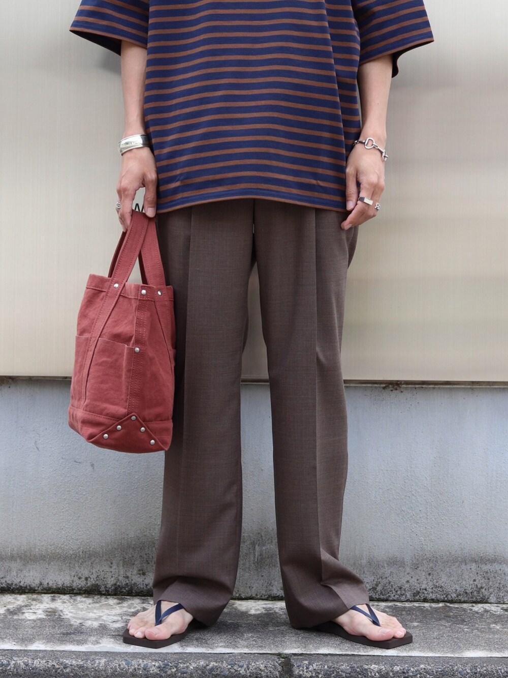 ブルー系のTシャツ/カットソー、ブラウン系のスラックス、レッド系のトートバッグを着用したメンズの夏コーディネートの4枚目の写真