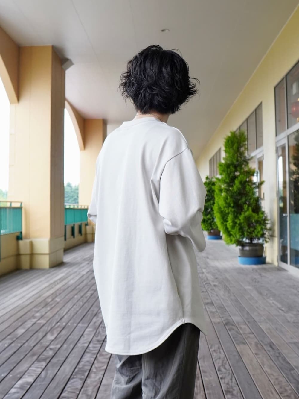 ホワイト系のTシャツ/カットソー、グレー系のスラックス、ブラック系のトートバッグを着用したメンズの夏コーディネートの2枚目の写真