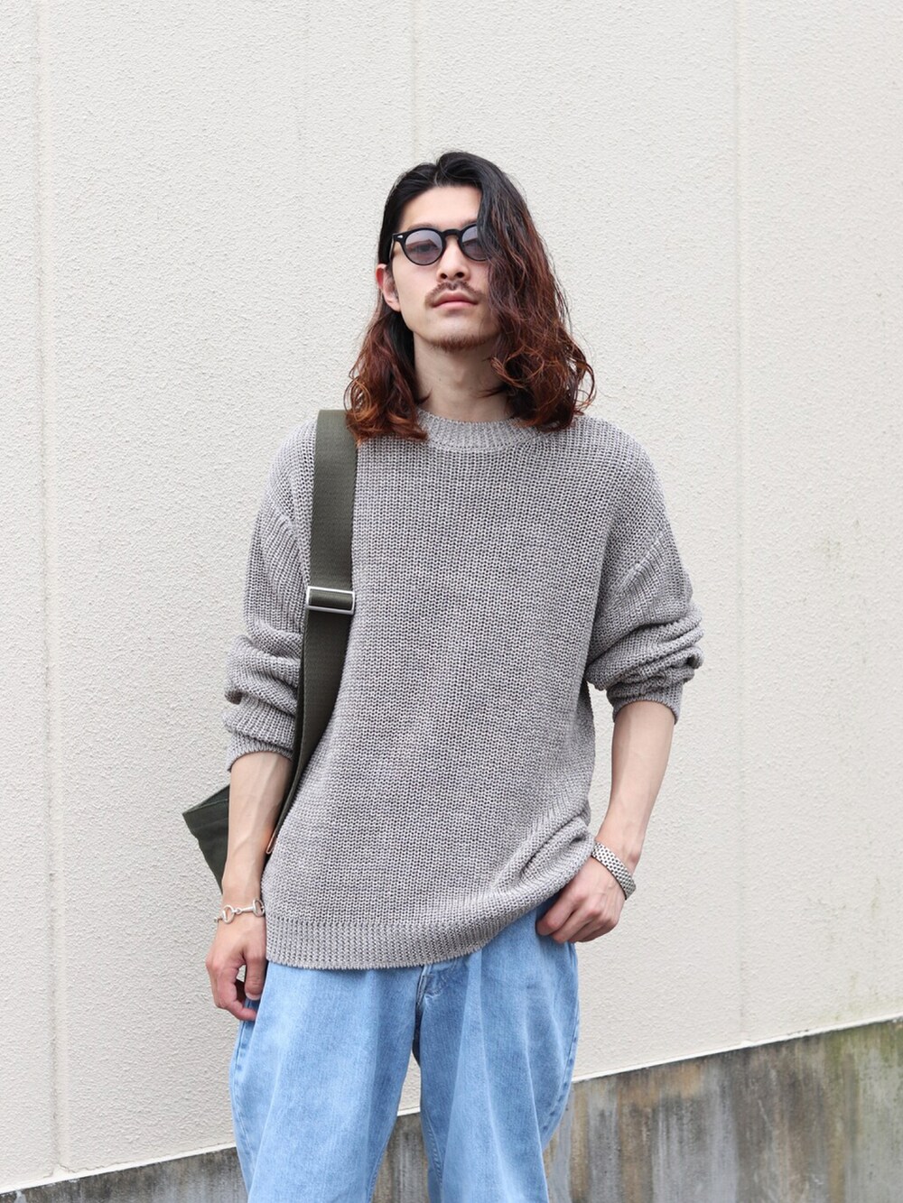 グレー系のニット/セーター、ブルー系のデニムパンツ、グリーン系のショルダーバッグを着用したメンズの夏コーディネートの2枚目の写真