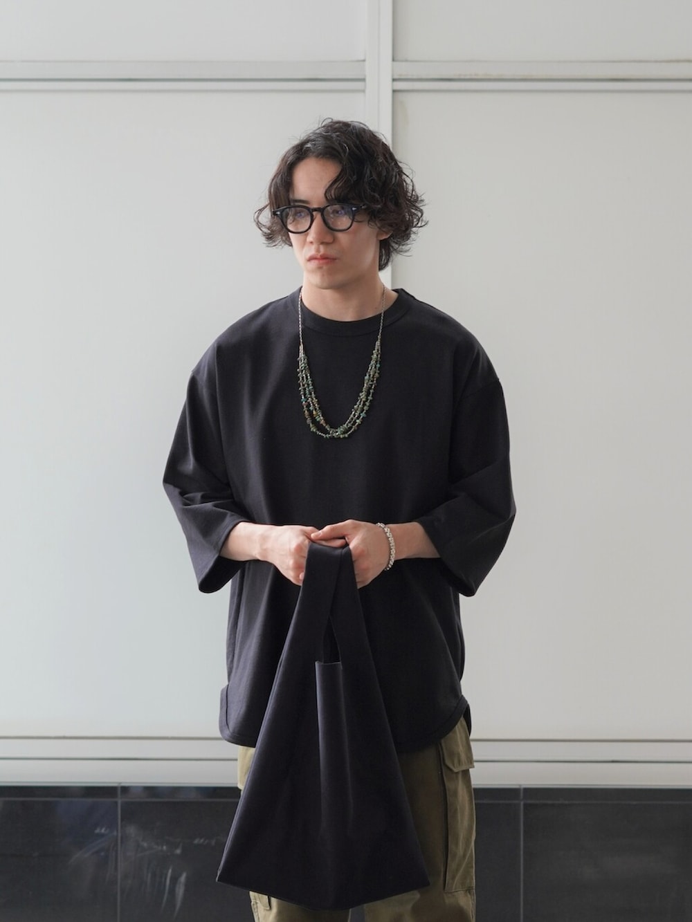 ブラック系のTシャツ/カットソー、グリーン系のカーゴパンツ、ブラック系のトートバッグを着用したメンズの夏コーディネートの2枚目の写真