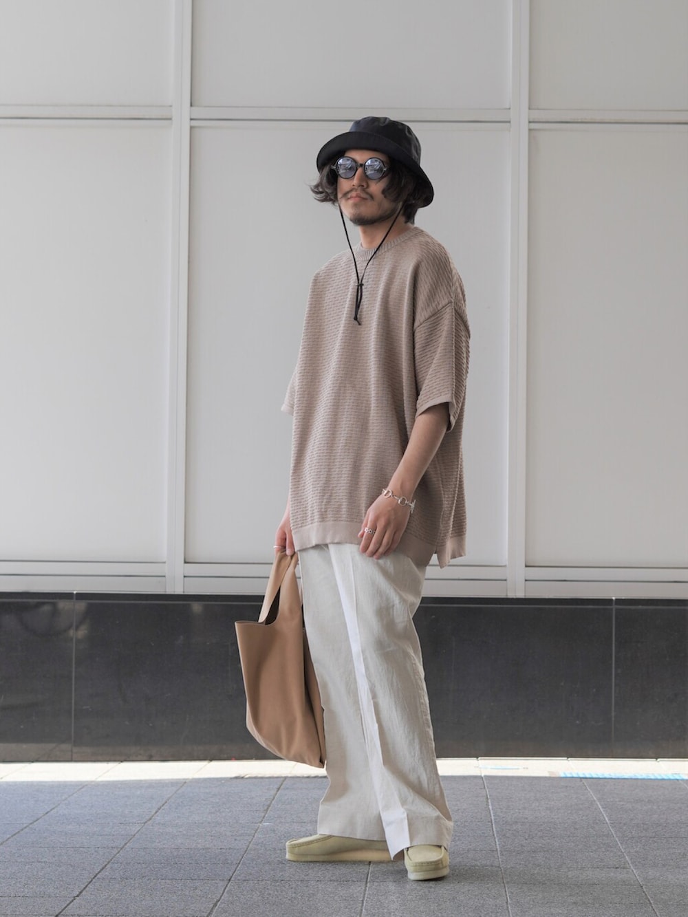 ブラウン系のトートバッグ、ベージュ系のTシャツ/カットソー、ベージュ系のスラックスを着用したメンズの春コーディネートの2枚目の写真